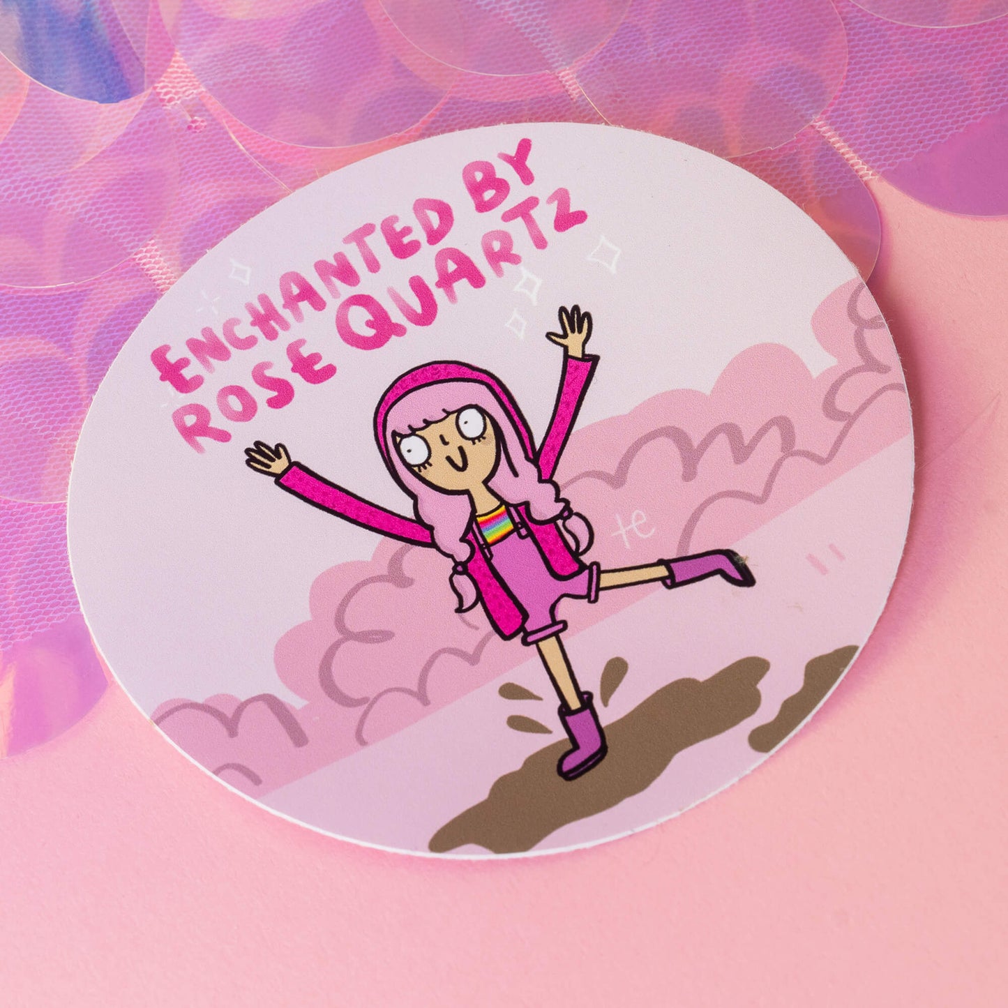 Circular sticker from Happiness Enchanters featuring an illustration of a character with pink hair, dressed in a pink outfit, jumping joyfully. The text 'Enchanted by Rose Quartz' is displayed above. The background includes whimsical clouds, and the image conveys a vibrant, playful energy. Happiness Enchanters blend art, writing, and alchemy to create magic through workshops and visual media.