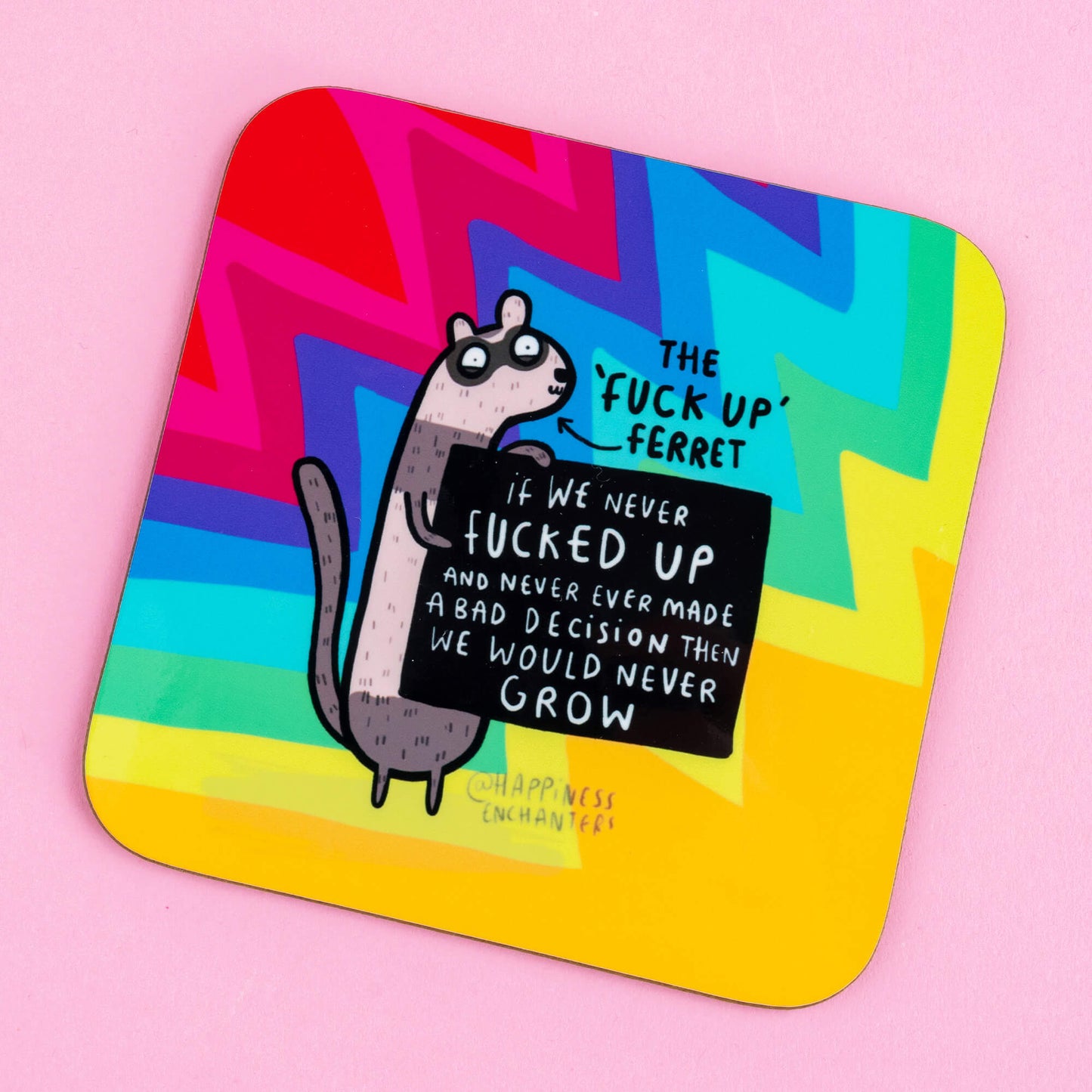 A close-up of a vibrant coaster from Happiness Enchanters depicting "The 'Fuck Up' Ferret" with a motivational message about learning from mistakes, set against a rainbow zigzag pattern.