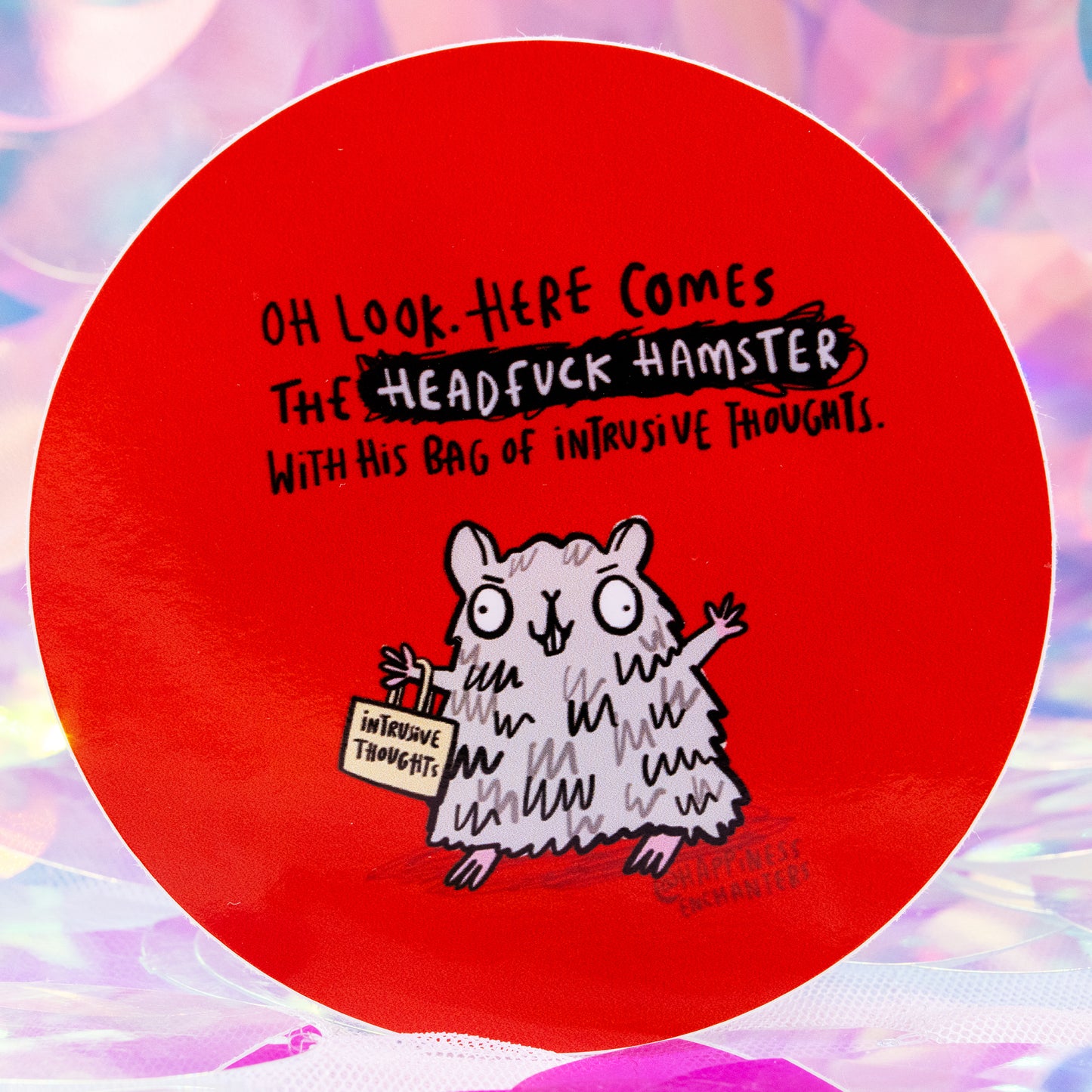 Close-up of the Headfuck Hamster Sticker by Happiness Enchanters. The bold red round sticker shows a cute wide-eyed grey hamster carrying a bag marked “intrusive thoughts”, paired with the text “Oh look. Here comes the Headfuck Hamster with his bag of intrusive thoughts.” Displayed on a shiny, pastel iridescent backdrop.