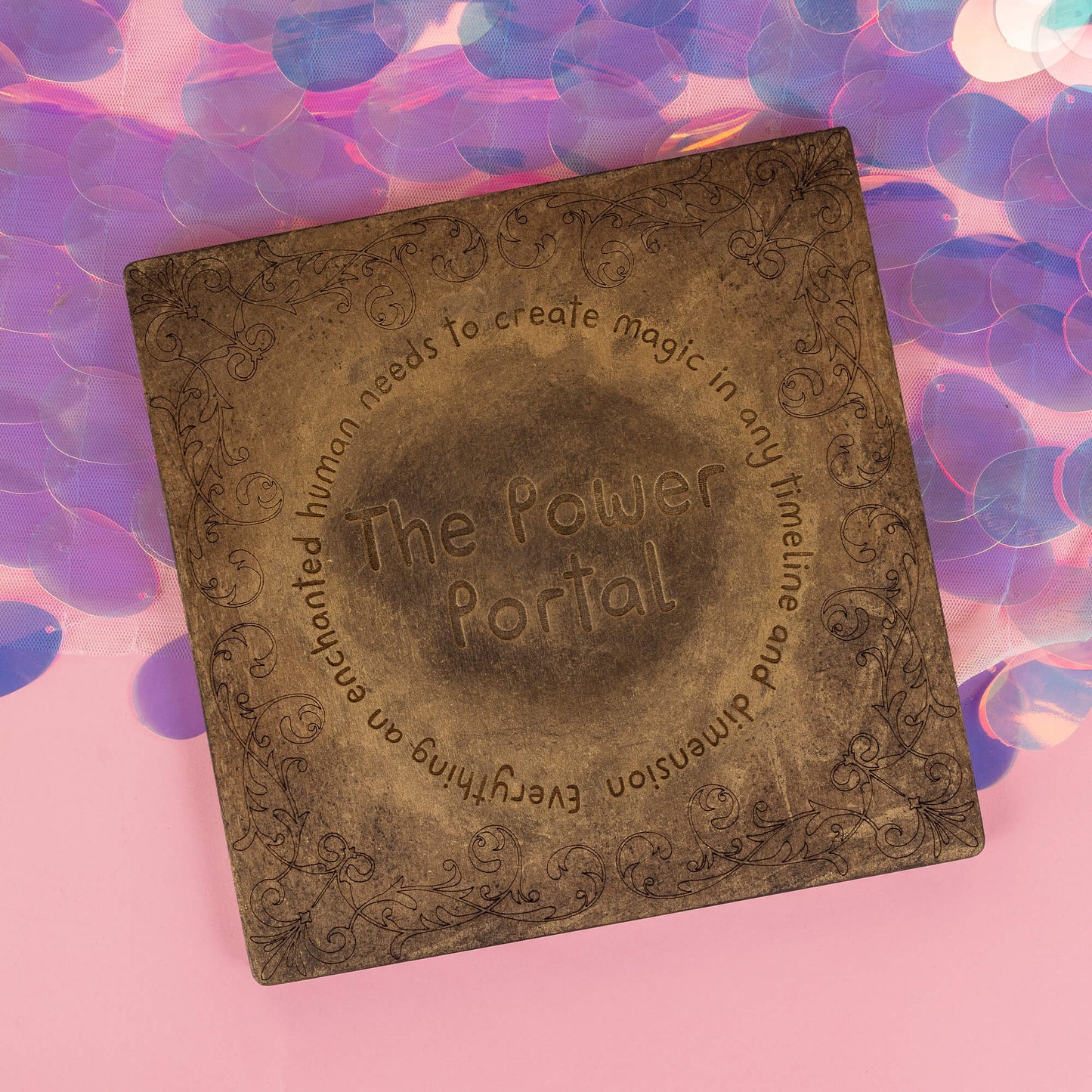 The Power Portal by Happiness Enchanters, a bronze-toned square board with intricate engraved designs, perfect for manifesting intentions and creating magic. The text reads, "The Power Portal – everything an enchanted human needs to create magic in any timeline and dimension." Set against a soft pink and iridescent background.
