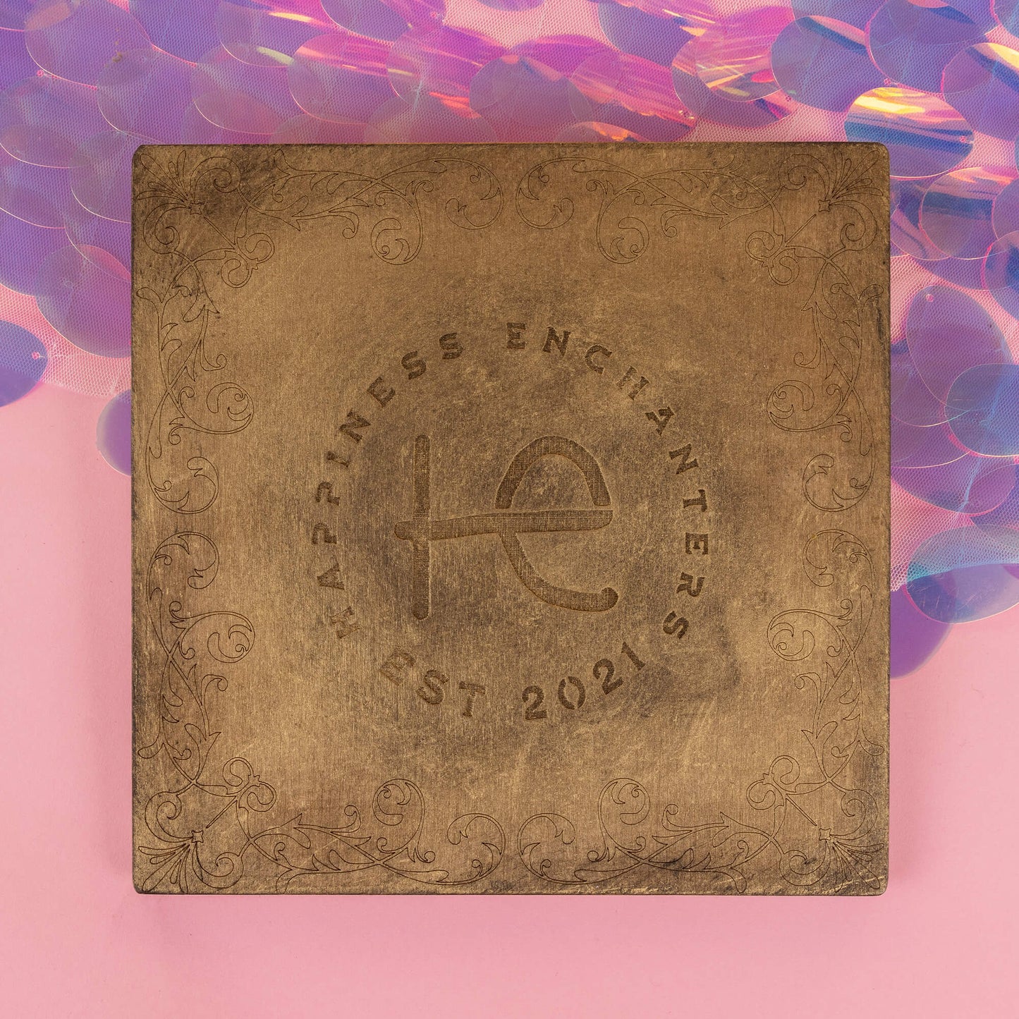 The back of the Power Portal by Happiness Enchanters, featuring a detailed engraving of the brand logo, "Happiness Enchanters Est 2021," with swirling patterns and a warm bronze finish. The iridescent backdrop adds a touch of magic to the mystical design.