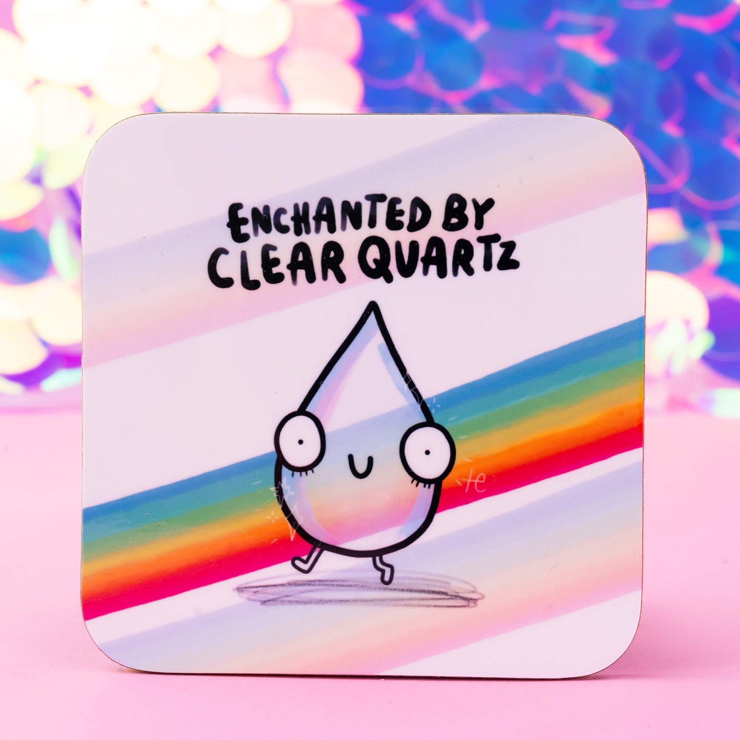 Happiness Enchanters coaster featuring a cute, smiling teardrop character with large eyes and a rainbow aura, set against a colourful background with the text 'Enchanted by Clear Quartz.' A whimsical design showcasing magic and creativity.