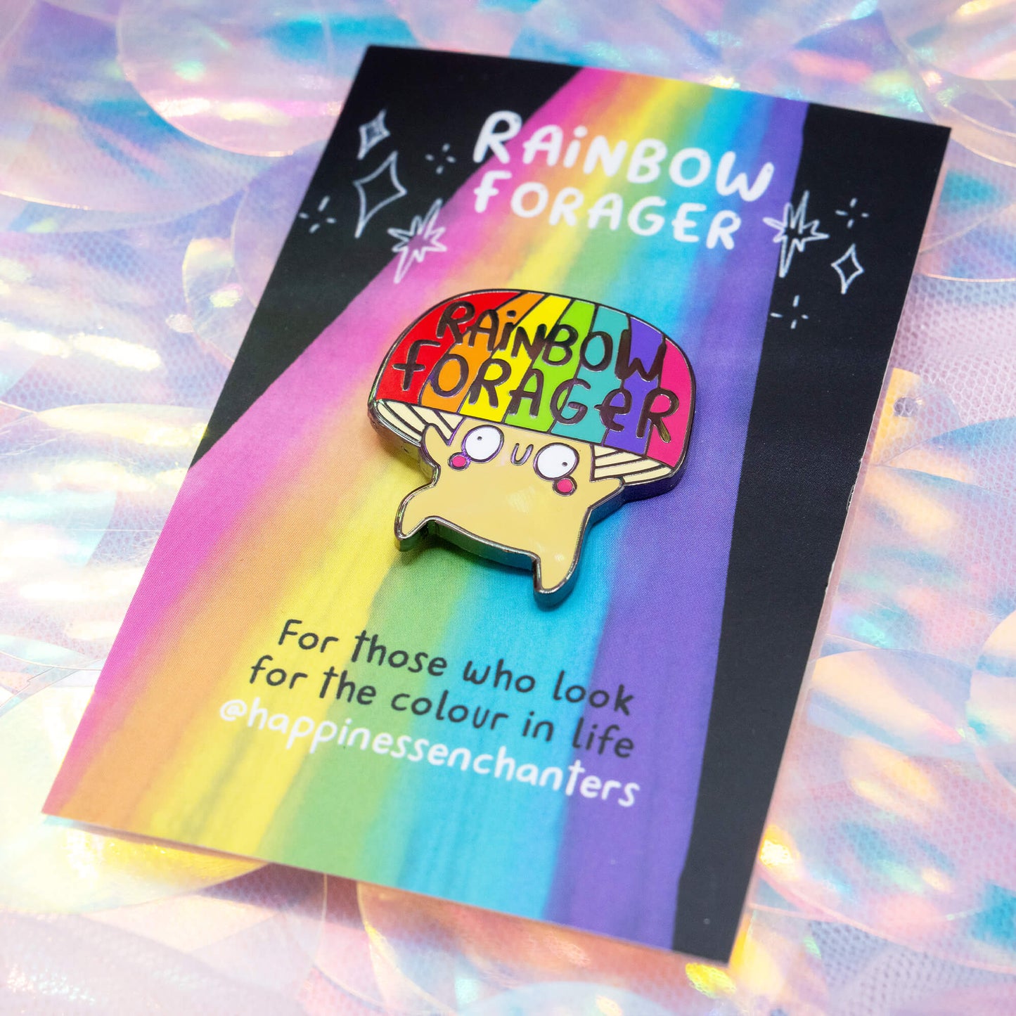 The Rainbow Forager Mushroom Pin Badge by Happiness Enchanters, featuring a cute illustrated mushroom with a rainbow hat and smiling face on a colourful backing card. A joyful accessory for those who love bright, magical art.