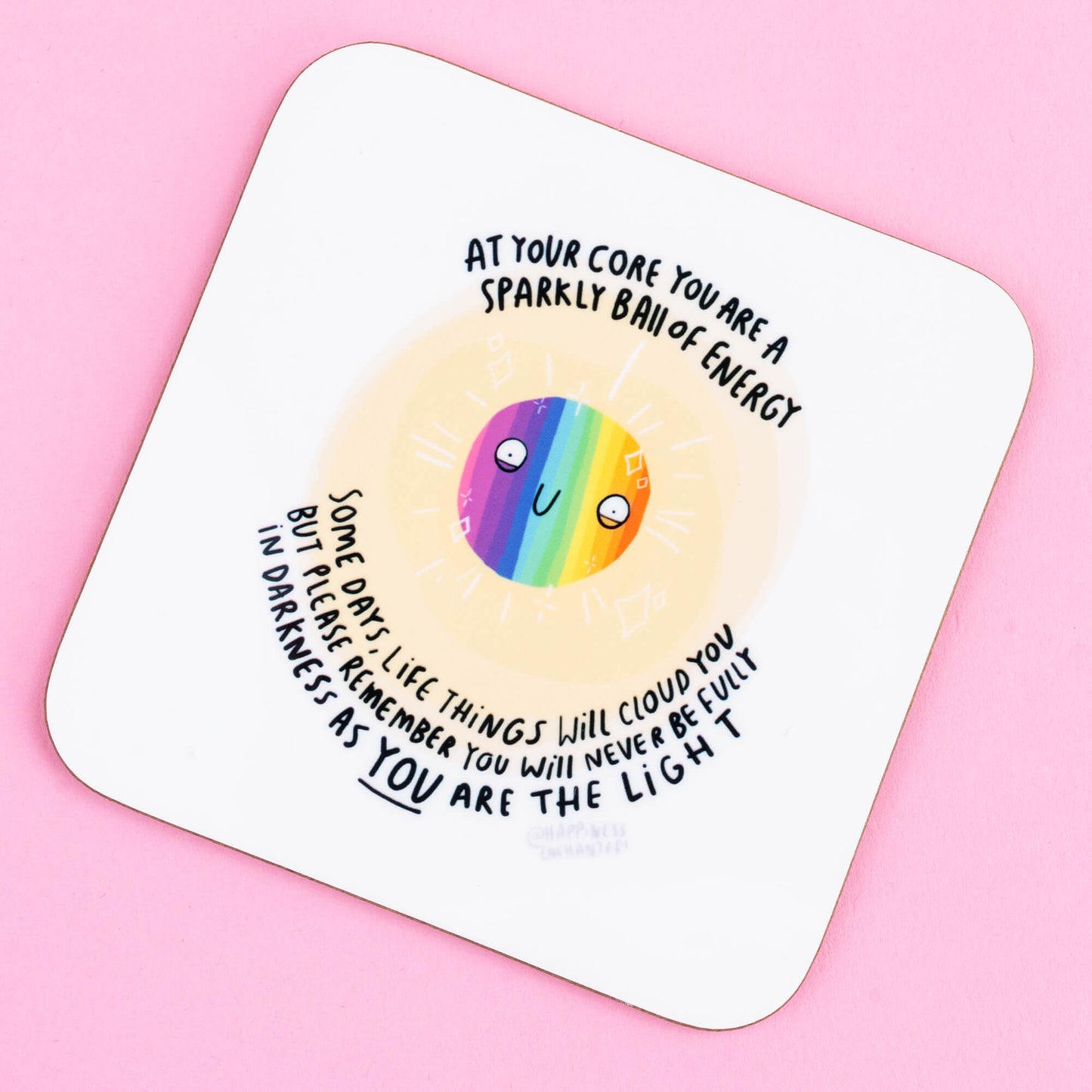 Square coaster by Happiness Enchanters, showcasing a rainbow-coloured happy face with an encouraging quote: 'At your core you are a sparkly ball of energy…you are the light.' Designed to spread positivity, this charming coaster adds a touch of magic to any space.