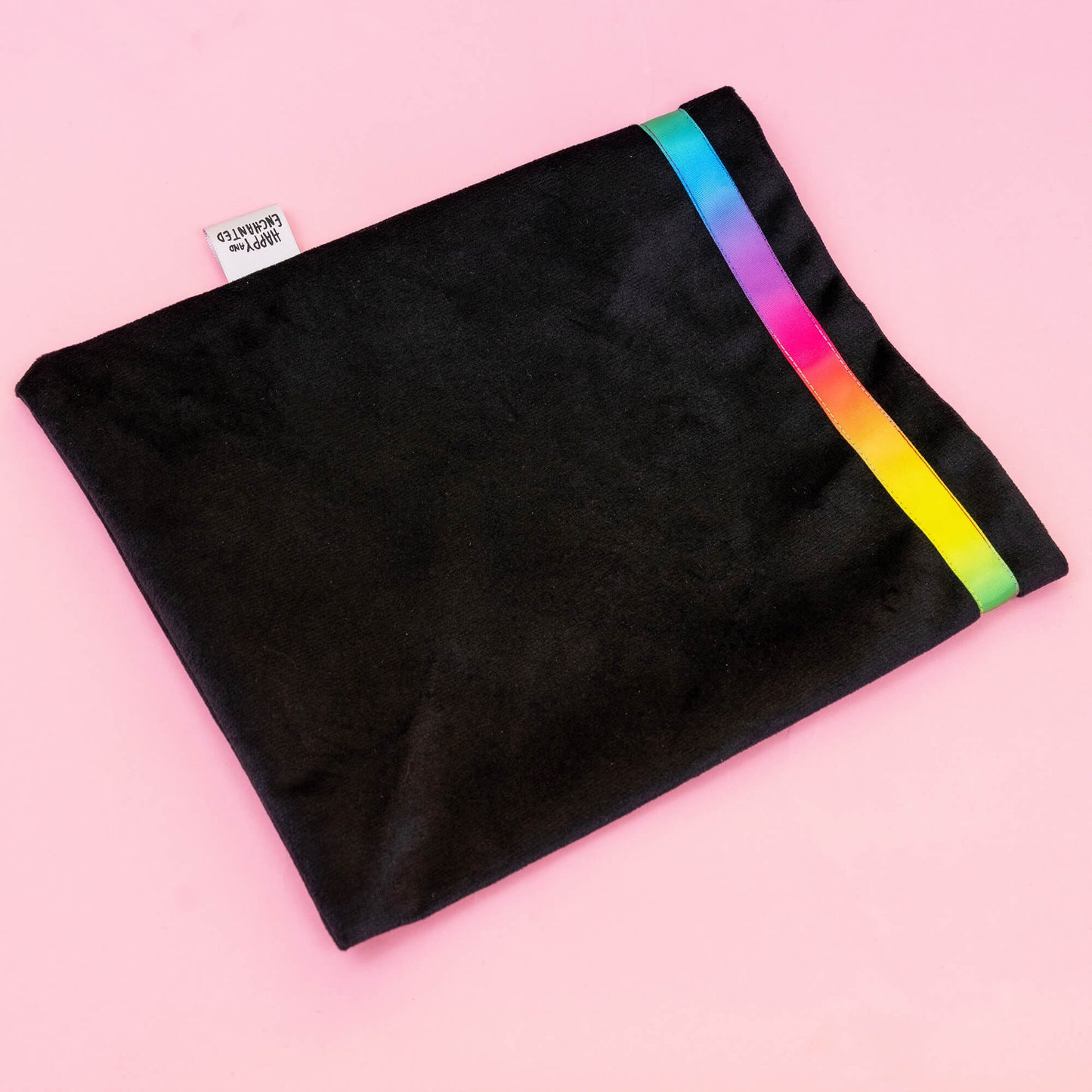 Happiness Enchanters black velvet bag with a vibrant rainbow trim, showcasing the brand’s elegant and magical aesthetic on a soft pink background. The bag represents a fusion of art and alchemy, embodying the brand’s ethos of creating magic through various forms of creativity and spiritual practices.