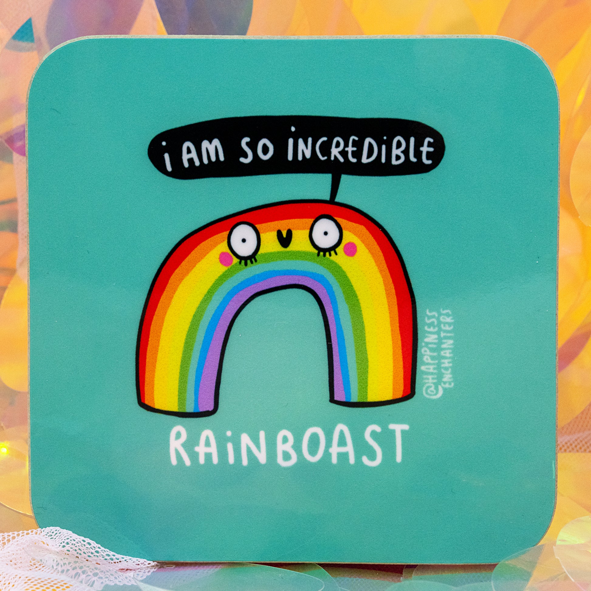 A colourful Rainboast coaster by Happiness Enchanters featuring a cute rainbow character with wide eyes and blushing cheeks on a teal background. The rainbow says “I am so incredible,” with the word Rainboast below. Designed by Katie Abey and Angela Sandland, this magical coaster adds joy, colour, and positivity to any space.