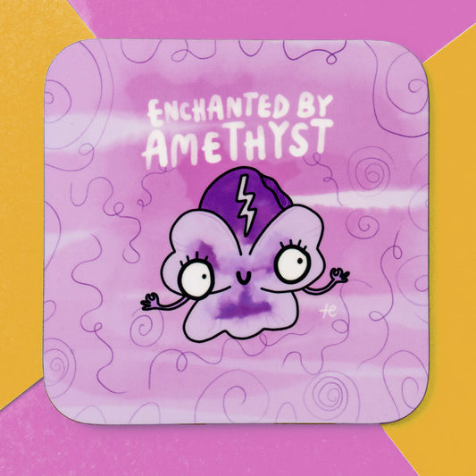 Vibrant coaster by Happiness Enchanters showcasing a cute amethyst character with expressive eyes and a lightning bolt on its head, set against a whimsical purple backdrop. The words 'Enchanted by Amethyst' appear above the character. The coaster is framed by a contrasting pink and yellow background. Perfect for creating a mystical vibe.