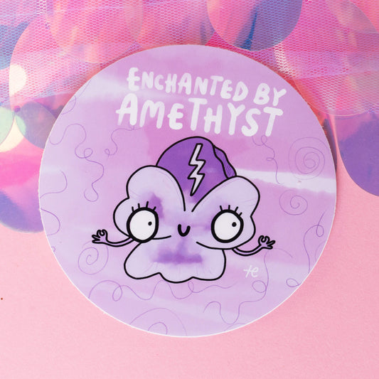 Happiness Enchanters' round sticker titled 'Enchanted by Amethyst,' depicting a cute, smiling amethyst character with wide eyes and a lightning bolt on its head. The design captures the brand's enchanting vibe, highlighting their dedication to art, magic, and creativity.