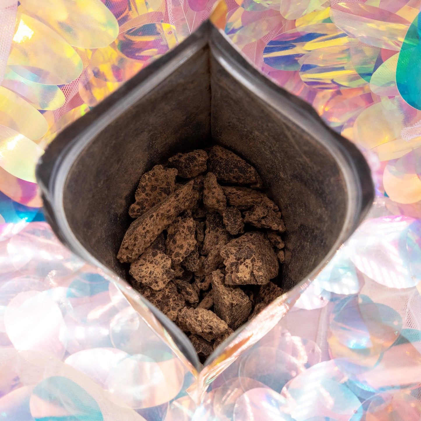 Close-up of Happy Heart of the Forest Ceremonial Cacao by Happiness Enchanters, showing rich, earthy cacao chunks inside a golden bag against a pastel iridescent background.