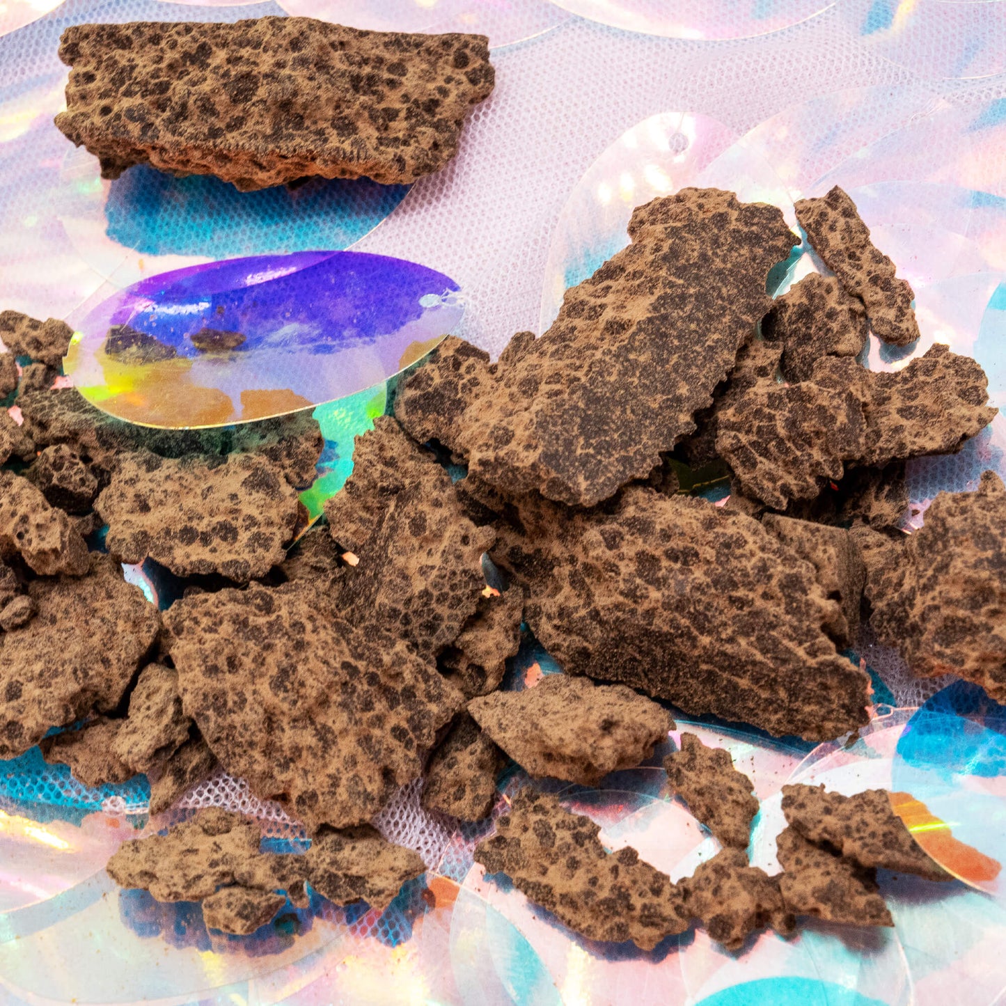 Detailed view of the cacao paste chunks from Happy Heart of the Forest Ceremonial Cacao by Happiness Enchanters, showing the textured, natural form on an iridescent surface.