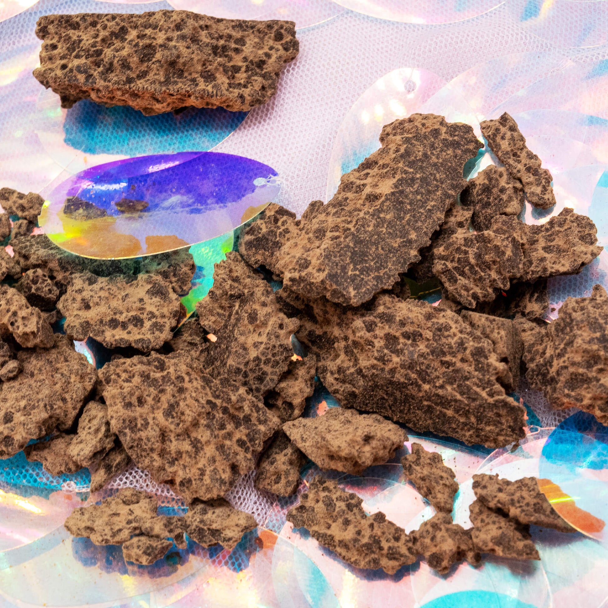Detailed view of the cacao paste chunks from Happy Heart of the Forest Ceremonial Cacao by Happiness Enchanters, showing the textured, natural form on an iridescent surface.