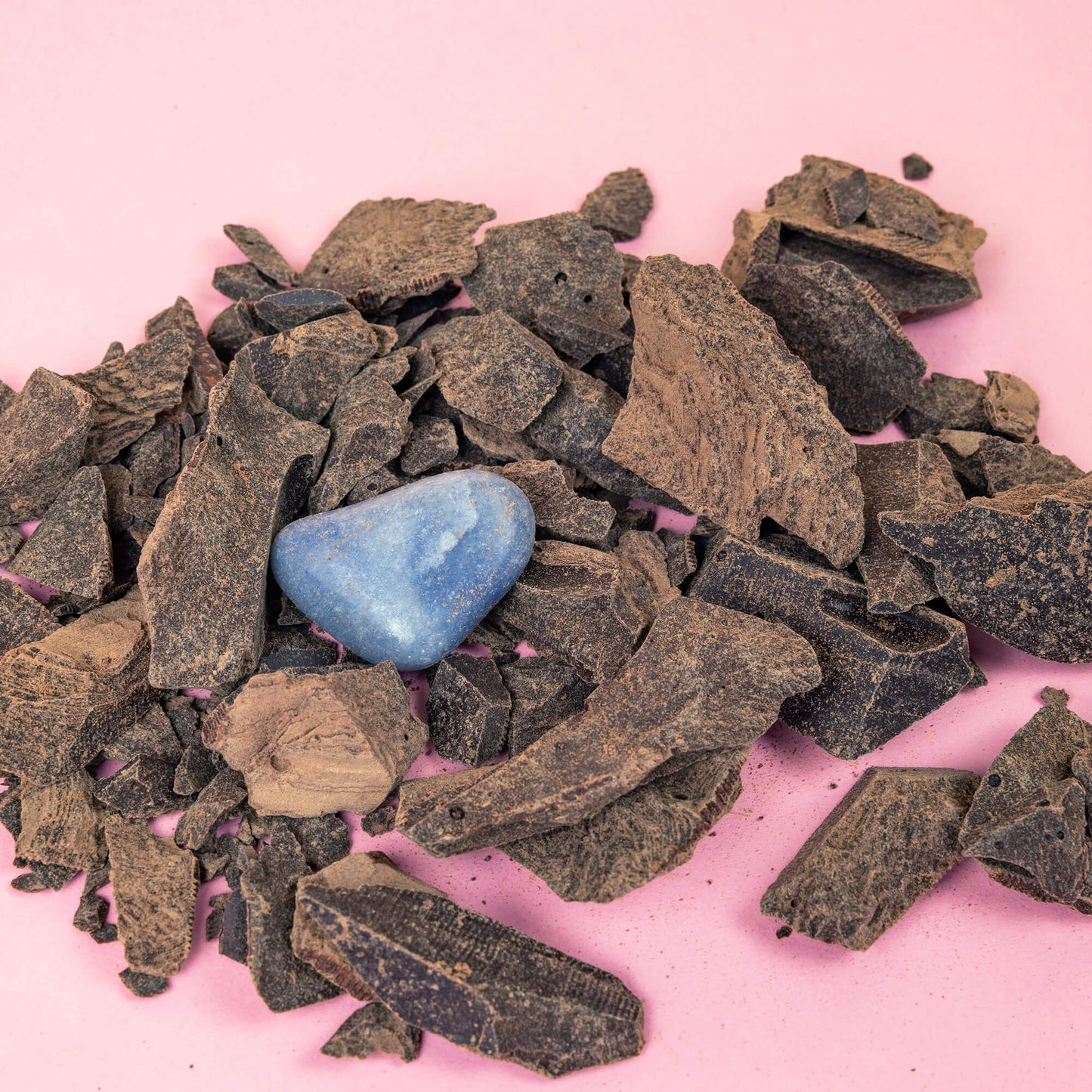  cacao nibs and a blue crystal on a pink surface.