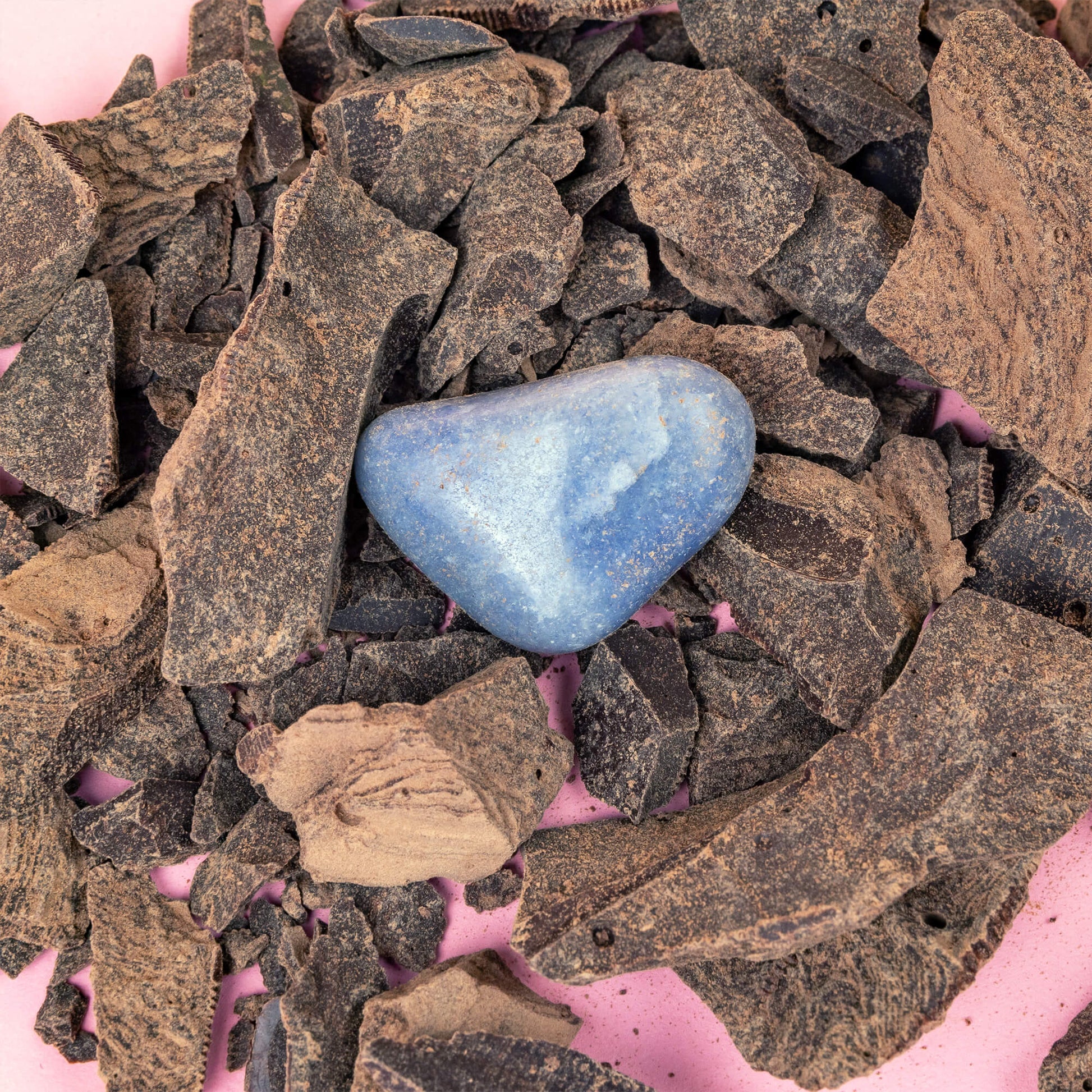 cacao nibs and a blue crystal on a pink surface.