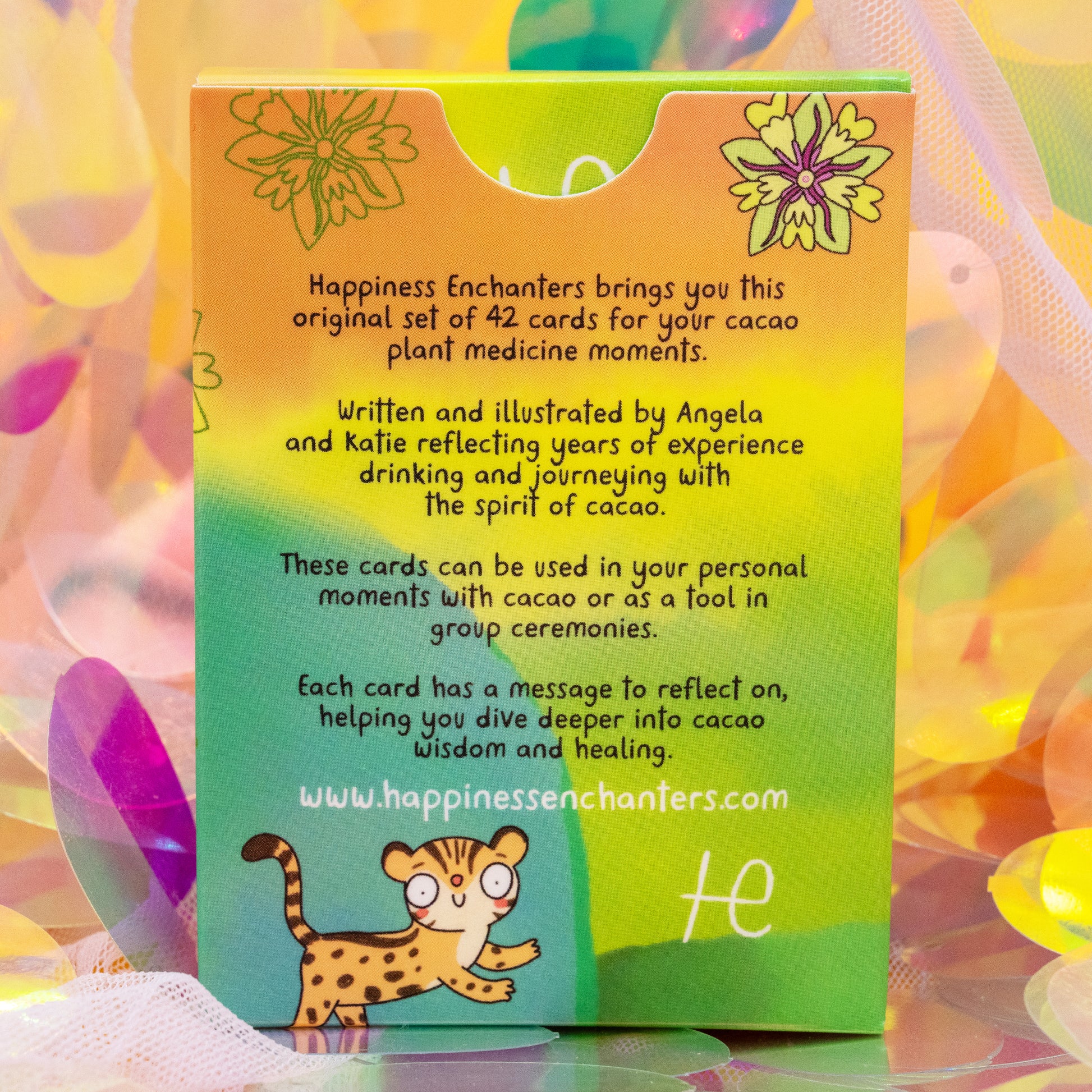 Back of the Cacao Journey Cards box by Happiness Enchanters with rainbow gradient colours and illustrated leopard. Text introduces the 42 card deck by Katie Abey and Angela Sandland for cacao ceremonies, meditation and spiritual reflection.