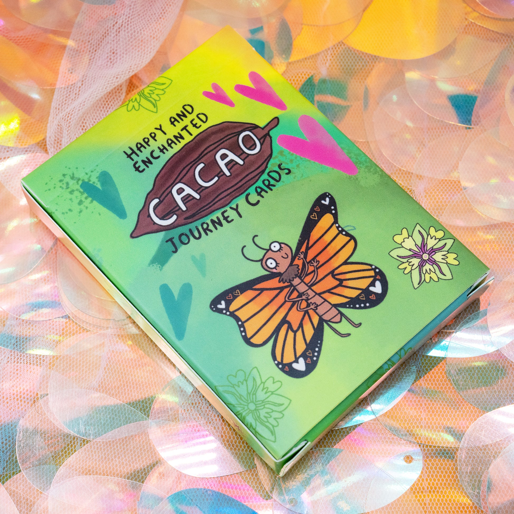 Front of the Cacao Journey Cards box by Happiness Enchanters, showing a cacao pod illustration and butterfly design. Created by Katie Abey and Angela Sandland, this colourful deck supports cacao rituals, meditation and plant medicine practice.