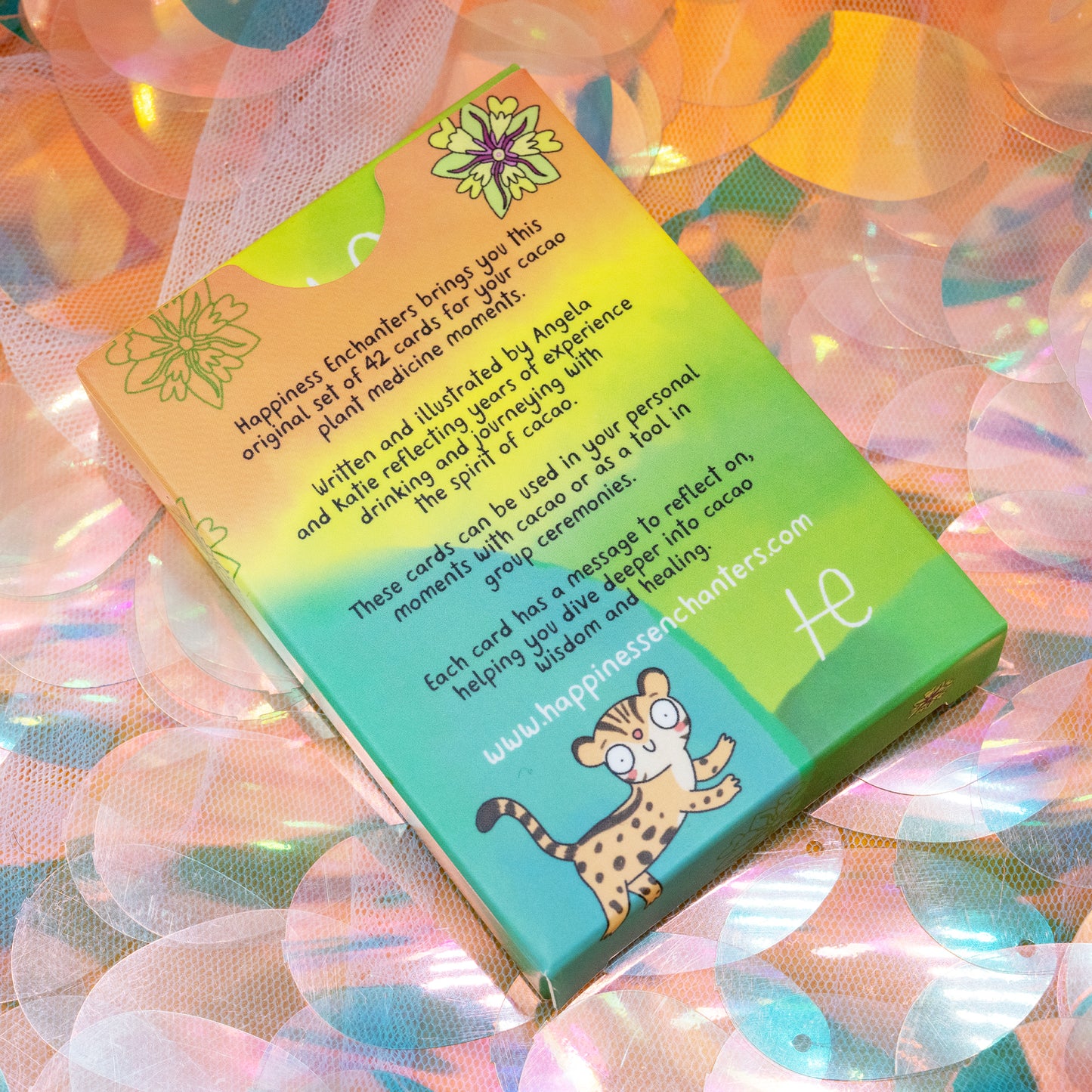 Back of the Cacao Journey Cards box by Happiness Enchanters, with bright rainbow colours and an illustrated leopard. Text describes the 42 card deck created by Katie Abey and Angela Sandland for cacao rituals, meditation and plant spirit journeys.