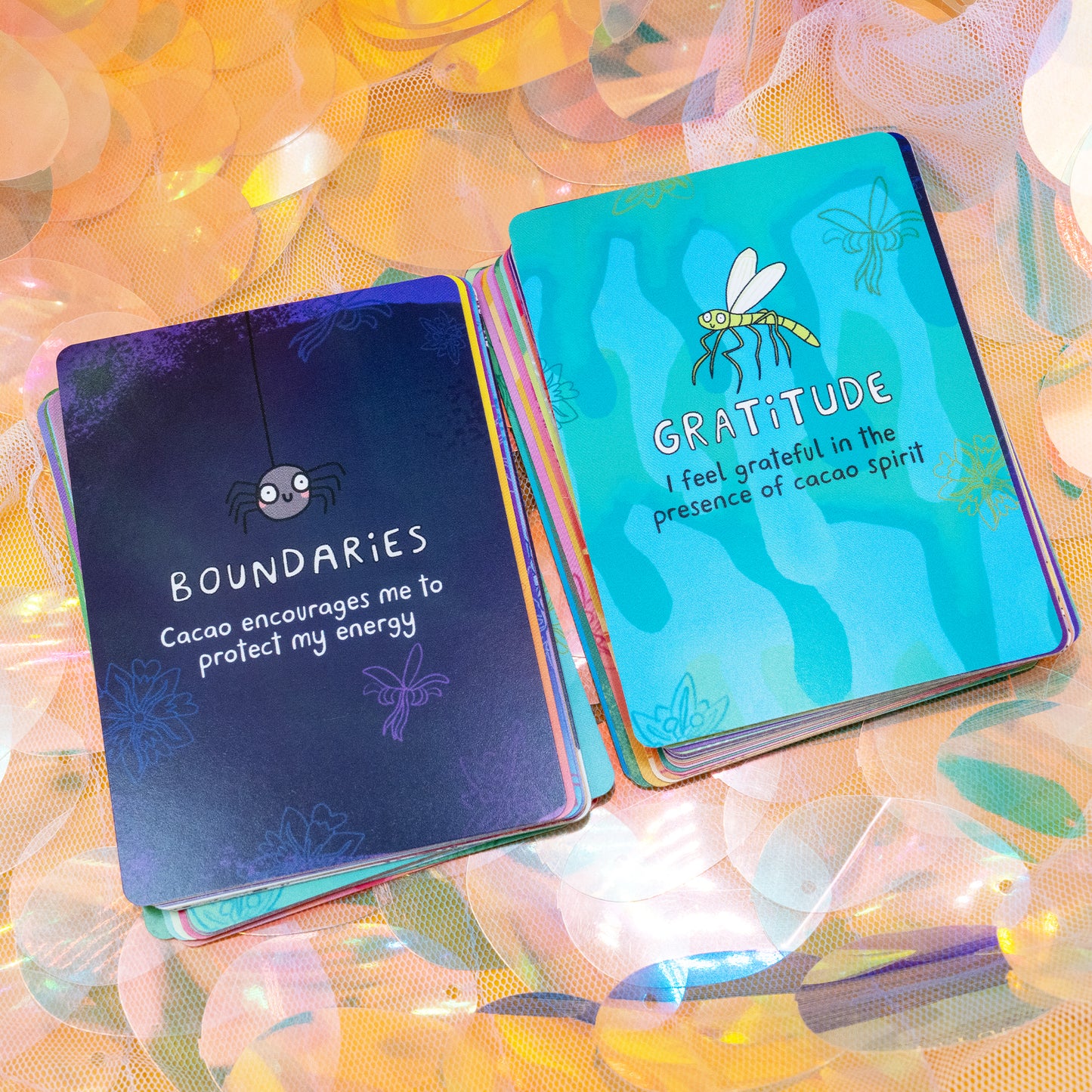 Two Cacao Journey Cards by Happiness Enchanters displayed on shimmering fabric, featuring the “Boundaries” and “Gratitude” cards with illustrated insects. Designed by Katie Abey and Angela Sandland for cacao rituals, mindfulness and spiritual practice.