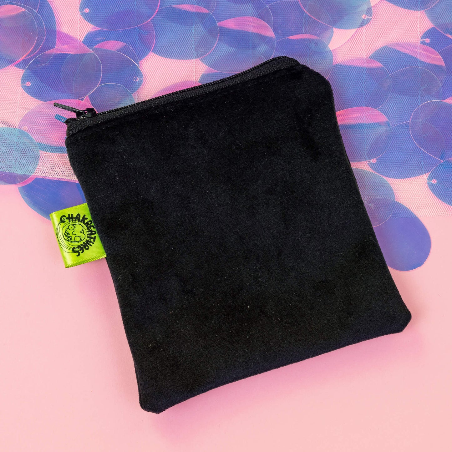 A black velvet pouch with a lime green Chakreatures logo tag, shown on a pastel pink background with iridescent accents. This sleek and simple pouch is designed to hold the Chakreatures cards by Happiness Enchanters, offering a secure and stylish way to keep your cards protected on-the-go.