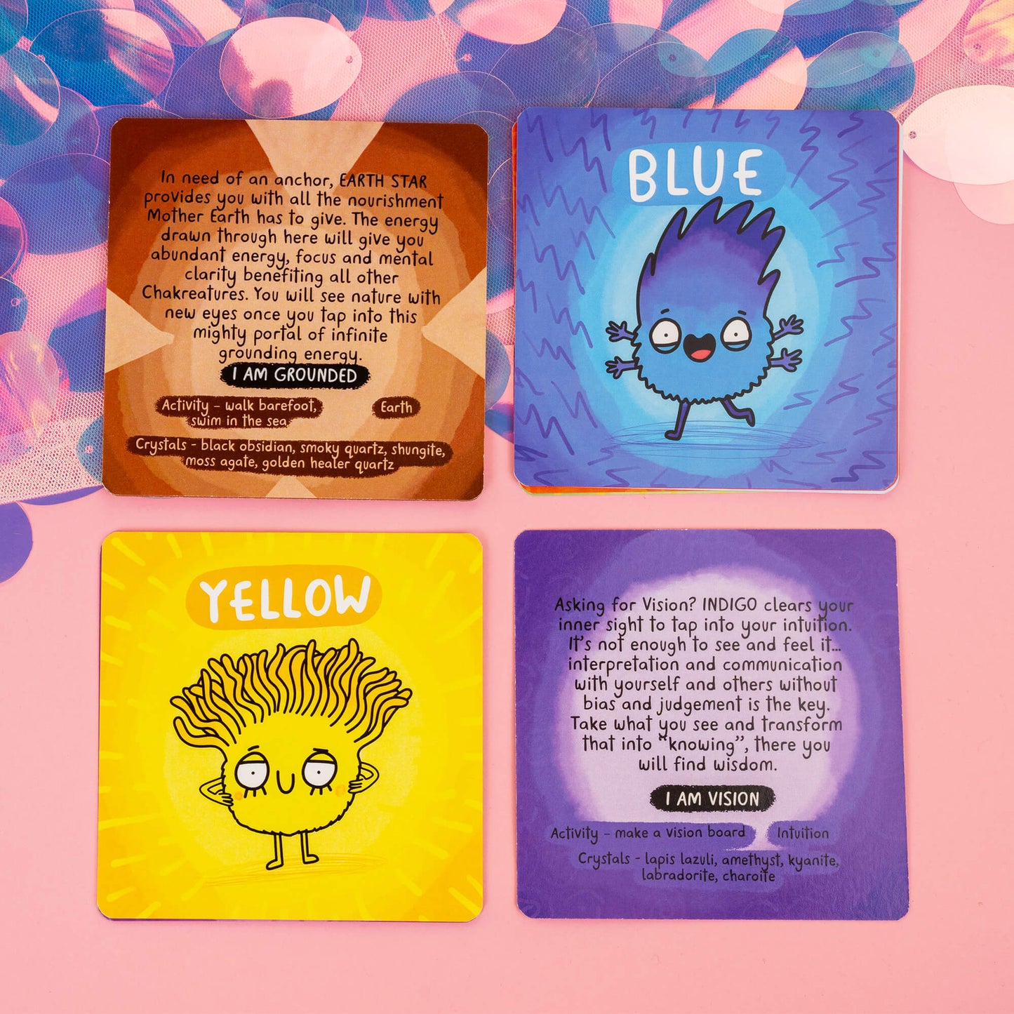 Four Chakreatures cards from Happiness Enchanters, each featuring a colourful character representing a different chakra. Cards include descriptions and affirmations like "I am Grounded" and "I am Vision," along with crystal and activity recommendations for chakra alignment. Set against a pink background with iridescent accents