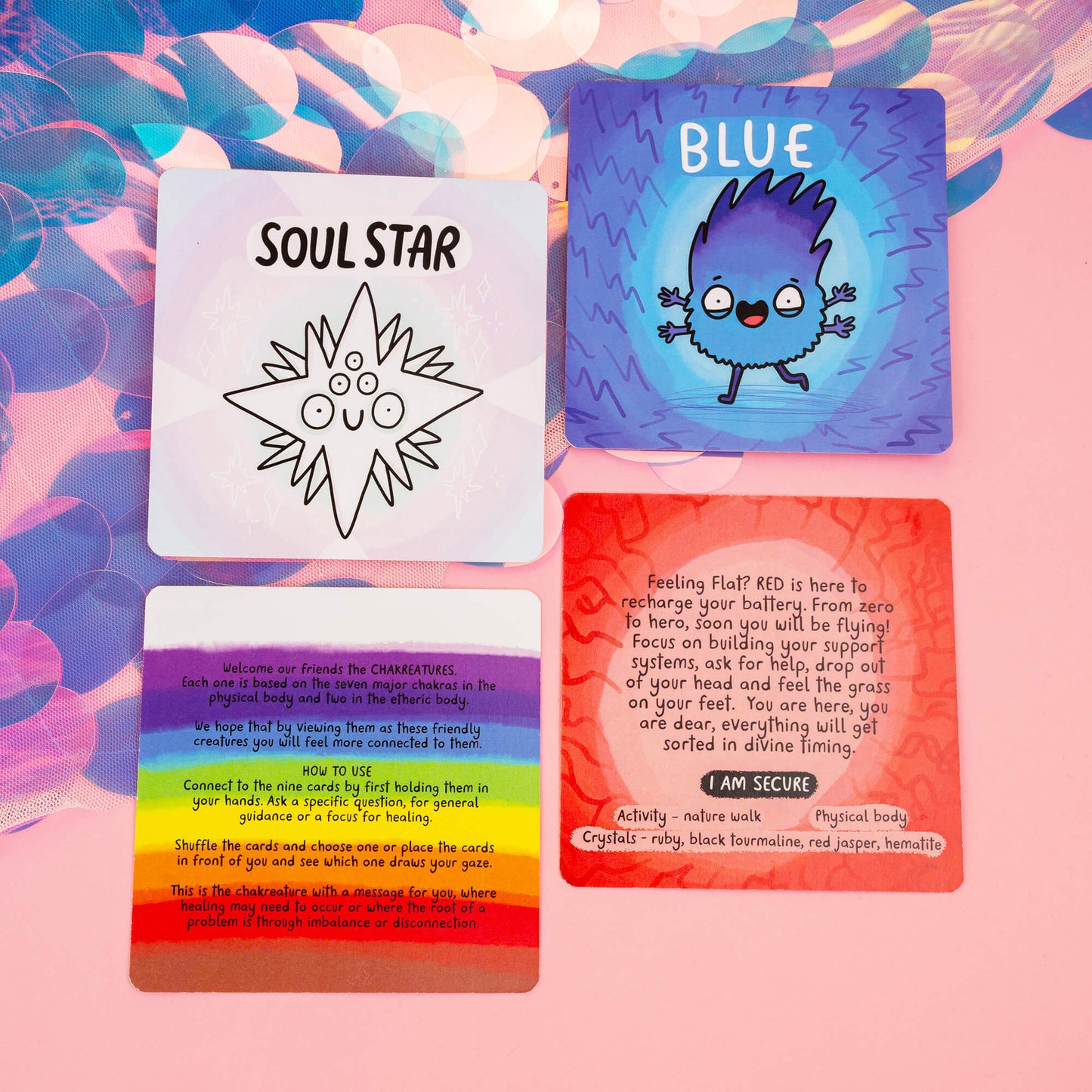 A selection of Chakreatures cards including the Soul Star, Blue, and Red chakras along with an instructional rainbow card. Each card provides unique guidance, activities, and crystals for chakra healing. Arranged on a pink background with iridescent details