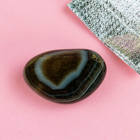 Happiness Enchanters agate crystal on a pink backdrop with metallic silver bag laid next to it