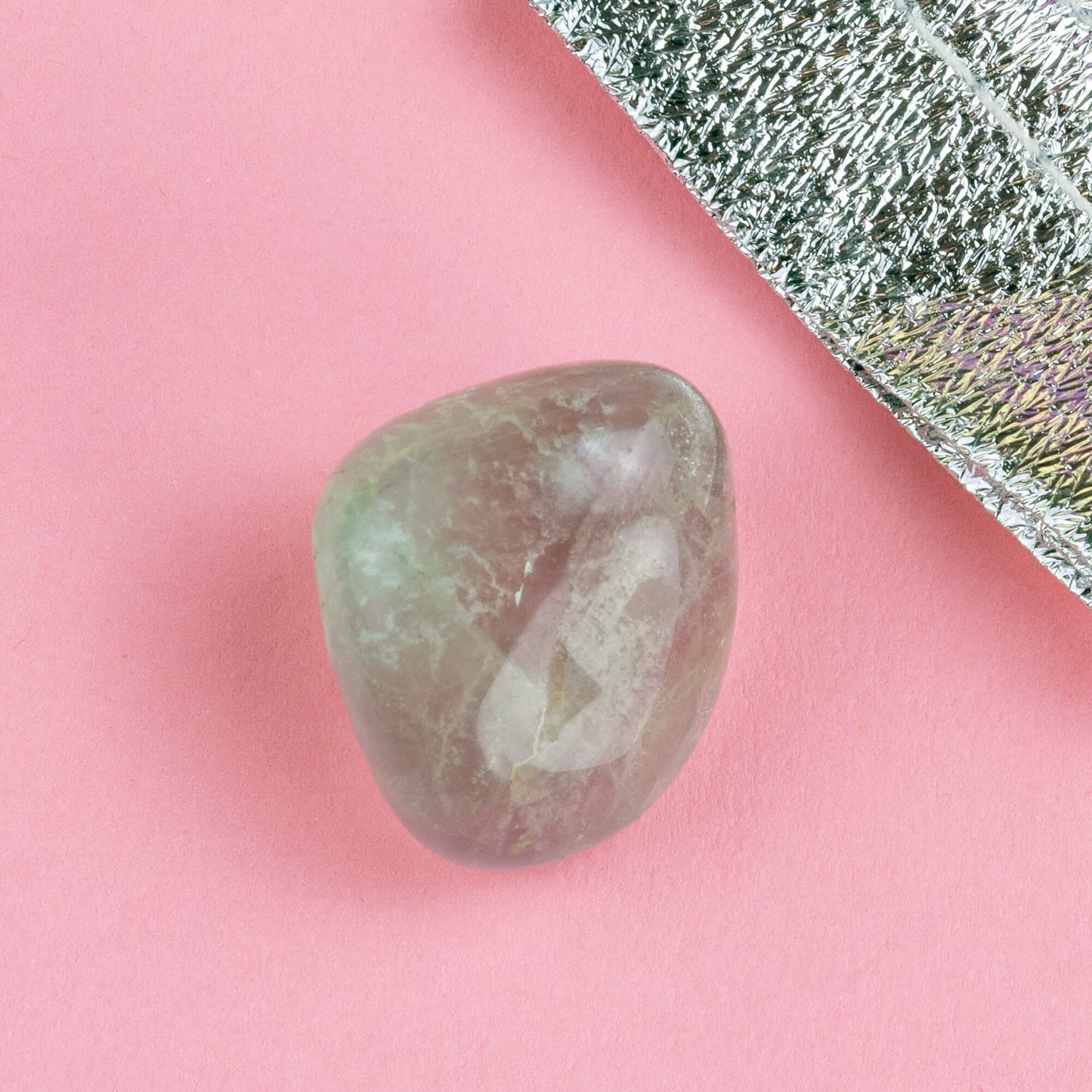 Happiness Enchanters Fluorite crystal on a pink backdrop with metallic silver bag laid next to it