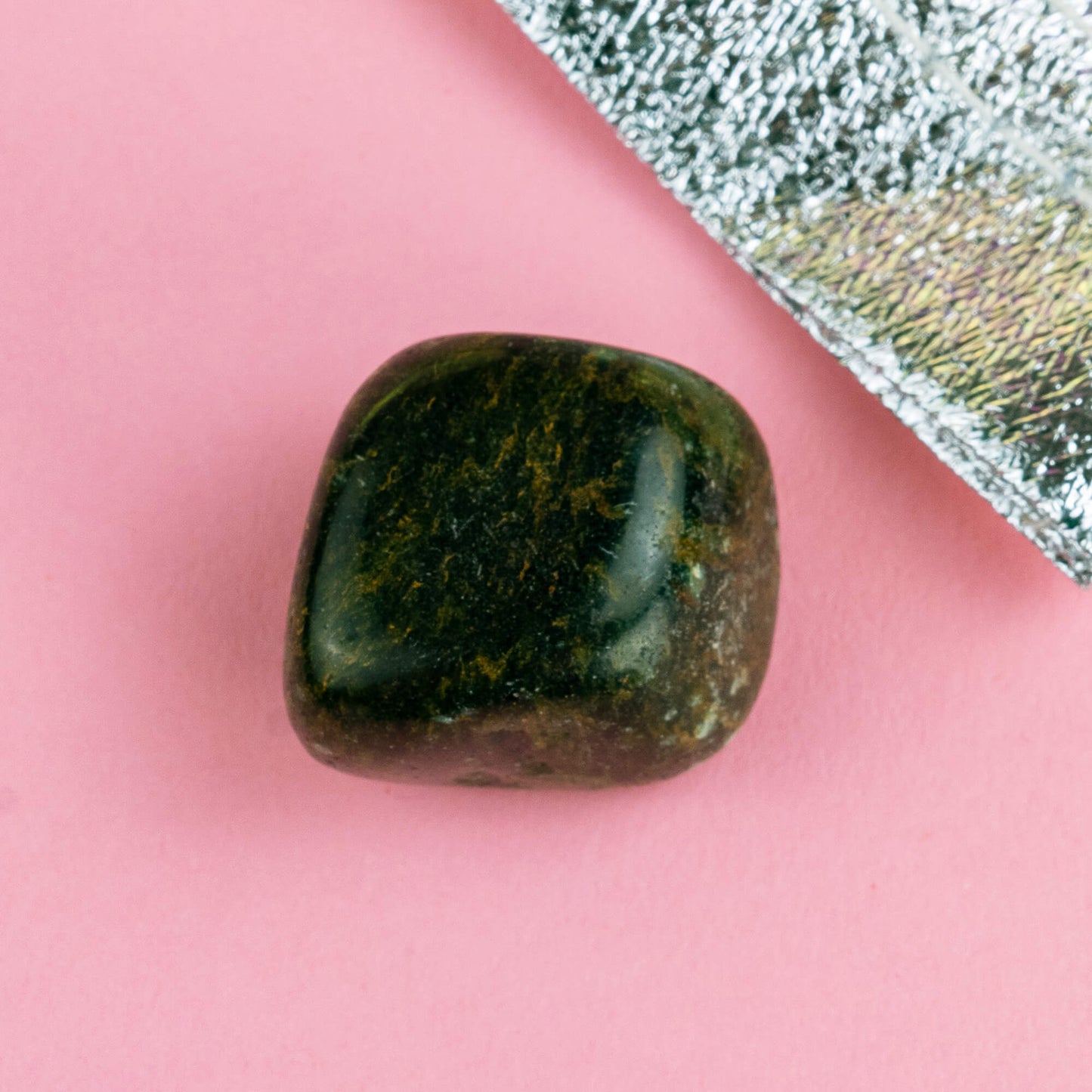 Happiness Enchanters nephrite jade crystal on a pink backdrop with metalic silver bag laid next to it