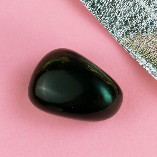 Happiness Enchanters smokey obsidian on a pink backdrop with metallic silver bag laid next to it