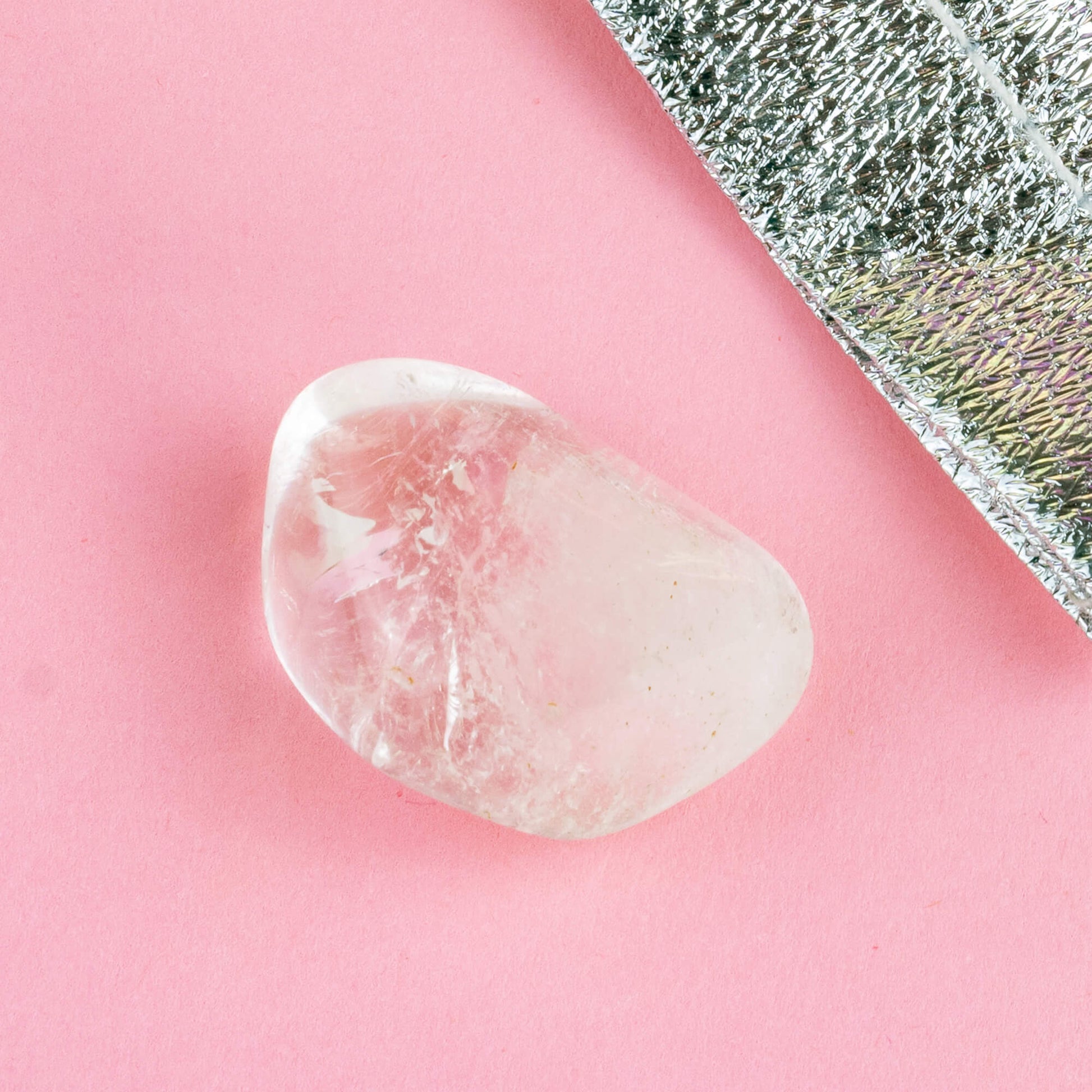 Happiness Enchanters clear quartz crystal on a pink backdrop with metallic silver bag laid next to it