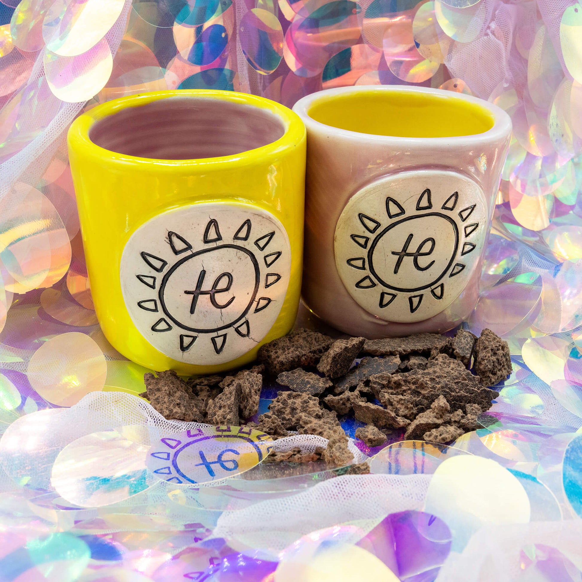 Happiness Enchanters yellow and pink ceramic cacao mugs displayed with cacao chunks, representing ritual cacao use.