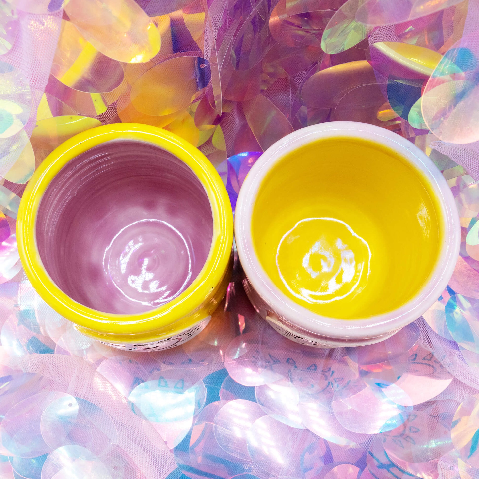 Overhead shot of two Happiness Enchanters cacao mugs, one yellow with pink interior and one pink with yellow interior.