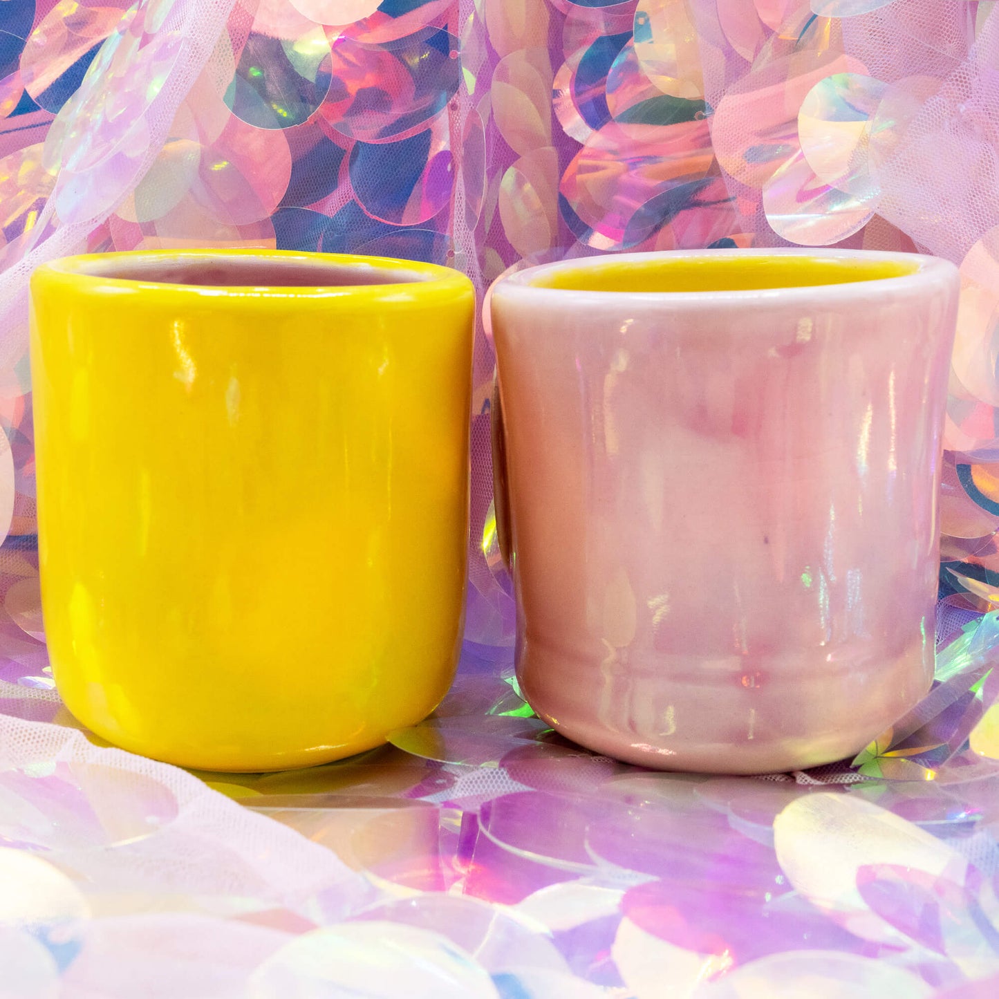 Yellow and pink Happiness Enchanters handmade mugs shown together with smooth glossy glaze and colourful backdrop.