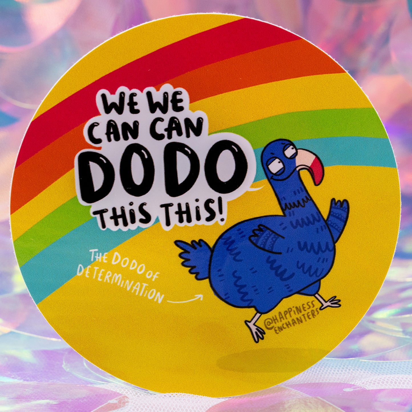 Close-up of the “We Can Dodo This!” rainbow sticker by Happiness Enchanters, designed by Katie Abey & Angela Sandland. Shows a cheerful blue dodo with the phrase “The Dodo of Determination”. Set on a bright, shimmering backdrop. Colourful motivational vinyl sticker for laptops, journals, and creative spaces.