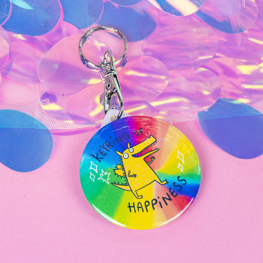 A keyring with a dragon  illustration on a rainbow base with sparkles and the keyring of happiness in text