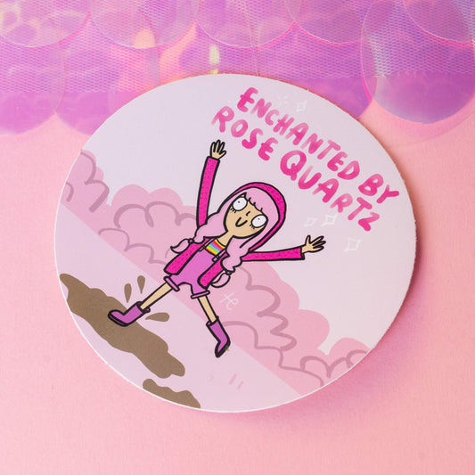 Round sticker by Happiness Enchanters showcasing a playful character with pink hair, wearing a pink outfit and boots, leaping with excitement. The text 'Enchanted by Rose Quartz' is prominently featured at the top. Surrounded by a dreamy cloud-filled background, the sticker represents the brand’s joyful and creative spirit. Happiness Enchanters craft magic through art, workshops, and holistic practices.