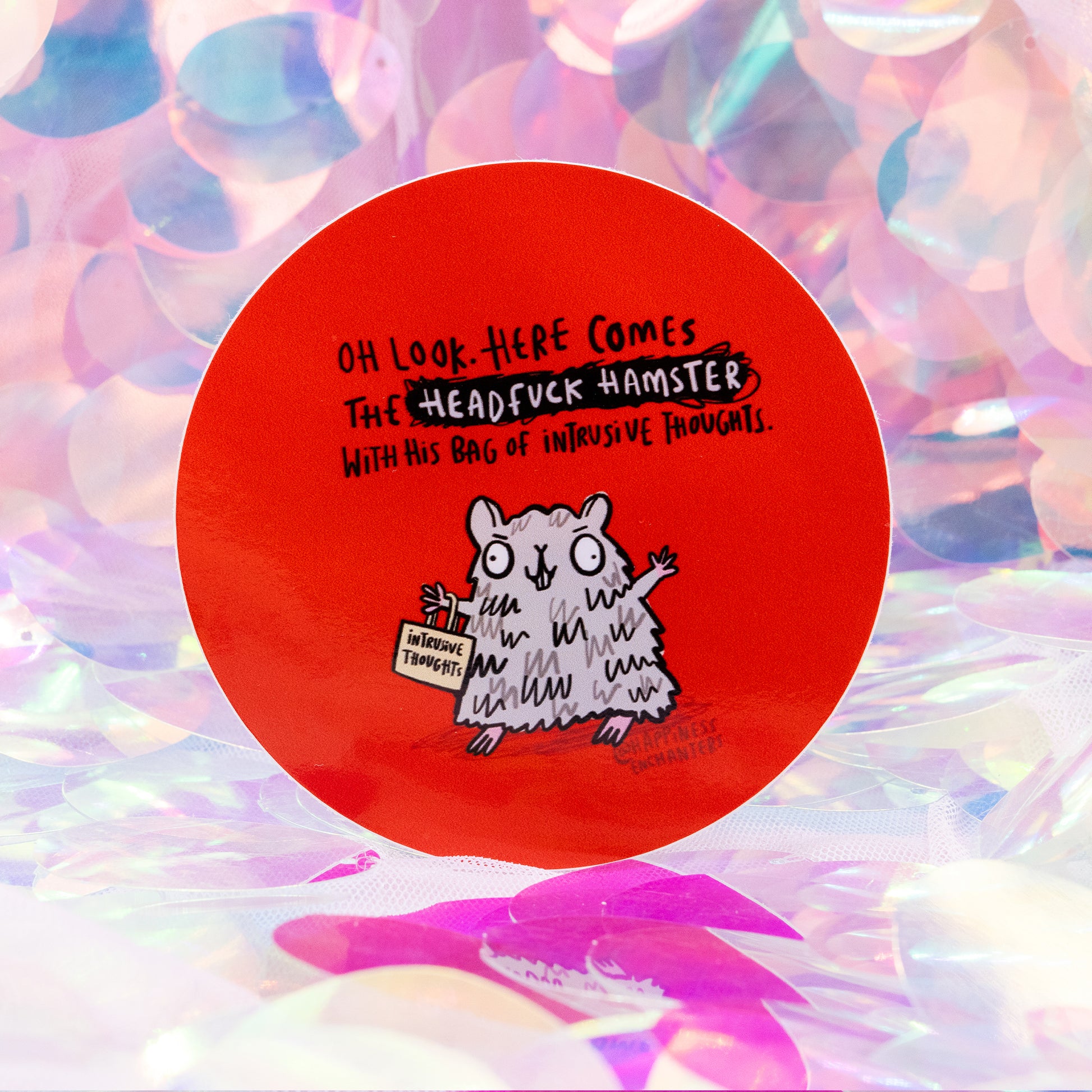 Round red sticker by Happiness Enchanters featuring a fluffy grey cartoon hamster holding a small bag labelled “intrusive thoughts”. Above it reads “Oh look. Here comes the Headfuck Hamster with his bag of intrusive thoughts.” Set against an iridescent pastel background. Humorous mental health themed sticker.