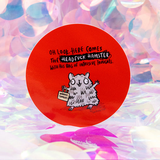 Round red sticker by Happiness Enchanters featuring a fluffy grey cartoon hamster holding a small bag labelled “intrusive thoughts”. Above it reads “Oh look. Here comes the Headfuck Hamster with his bag of intrusive thoughts.” Set against an iridescent pastel background. Humorous mental health themed sticker.