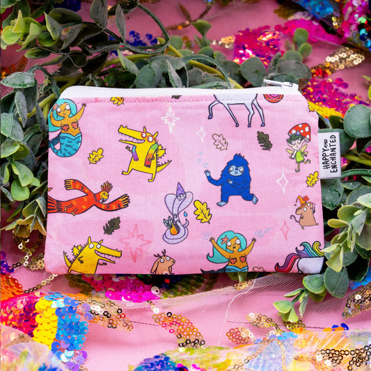 Pink 'Word Spells' coin purse by Happiness Enchanters, featuring whimsical characters like mermaids, dragons, fairies, and forest creatures, drawn by Katie Abey and Angela Sandland. Handmade with a unique fabric section, finished with a 'Happy and Enchanted' tag. Surrounded by greenery and colourful sequins.