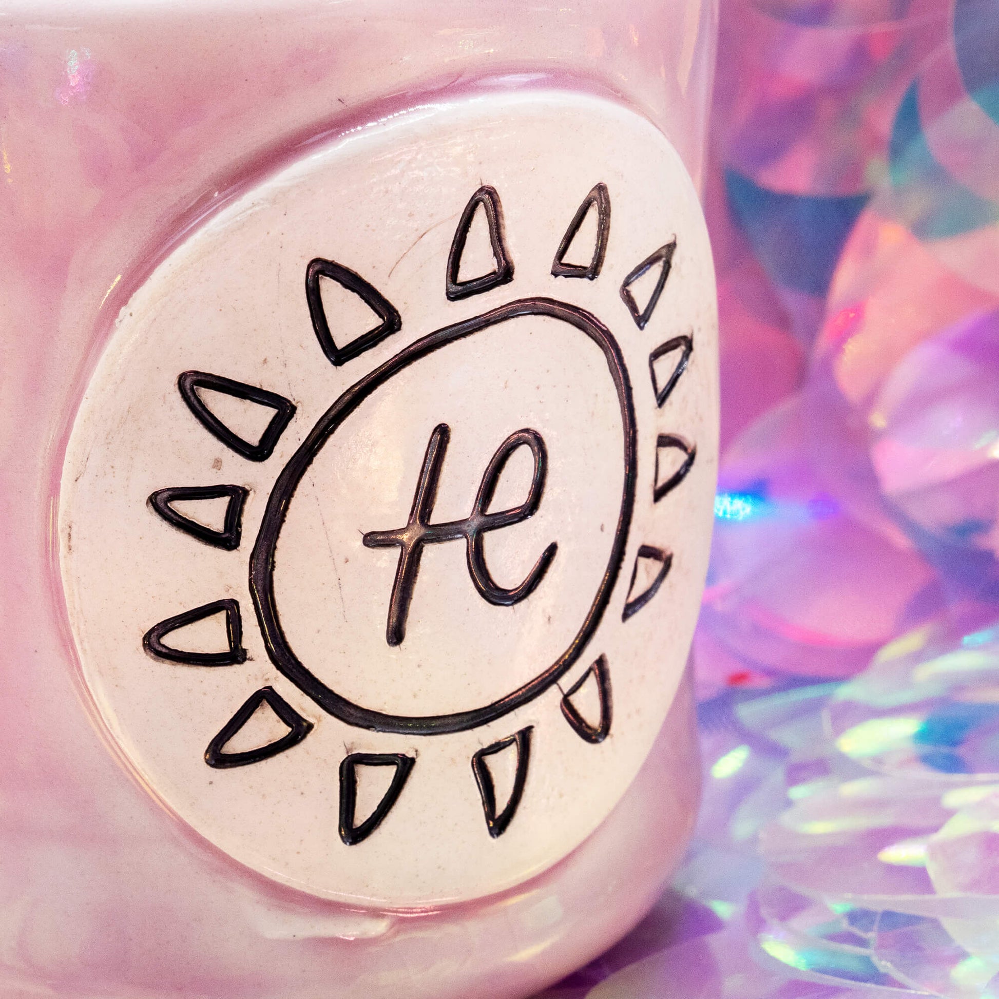 Close-up of the pale pink Happiness Enchanters ceramic mug showing the hand-carved sun and symbol design.