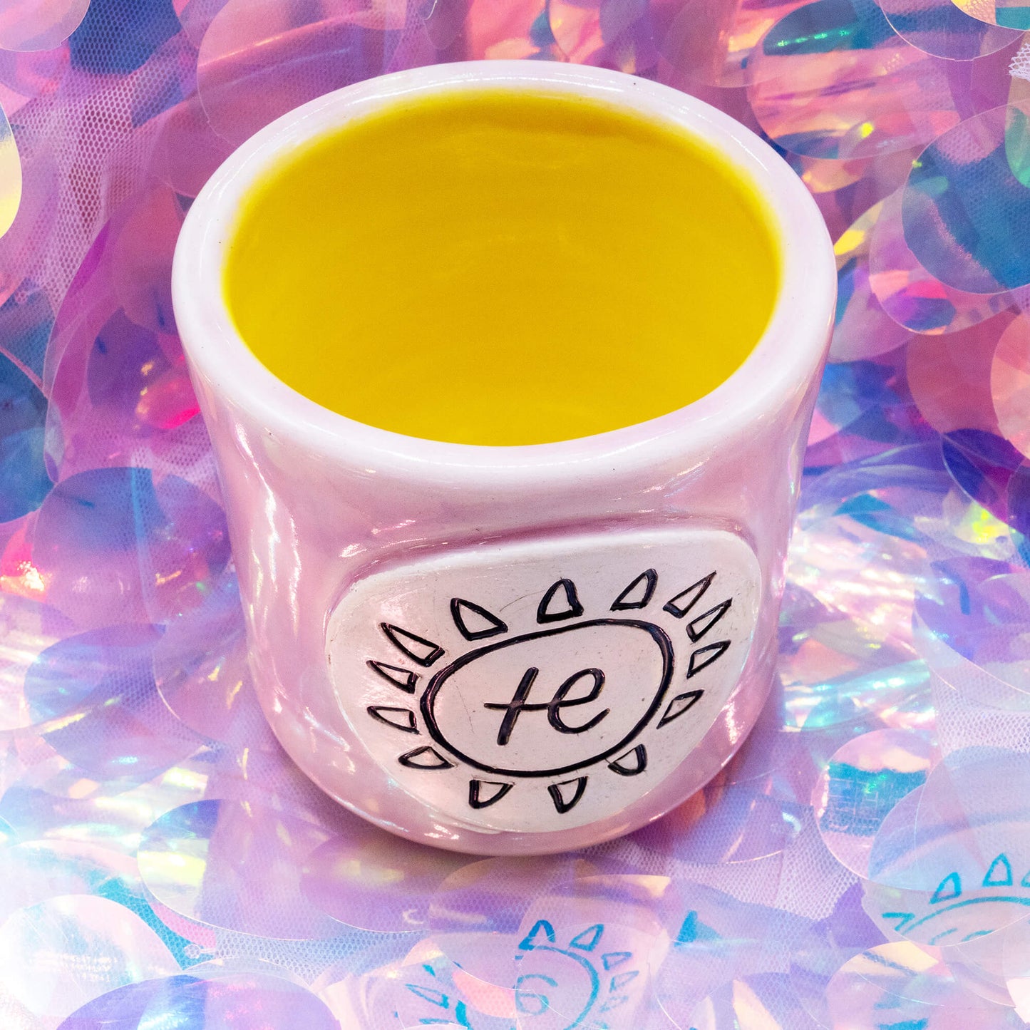 Overhead view of the pink Happiness Enchanters handmade ceramic cacao cup with yellow interior on an iridescent pastel background.
