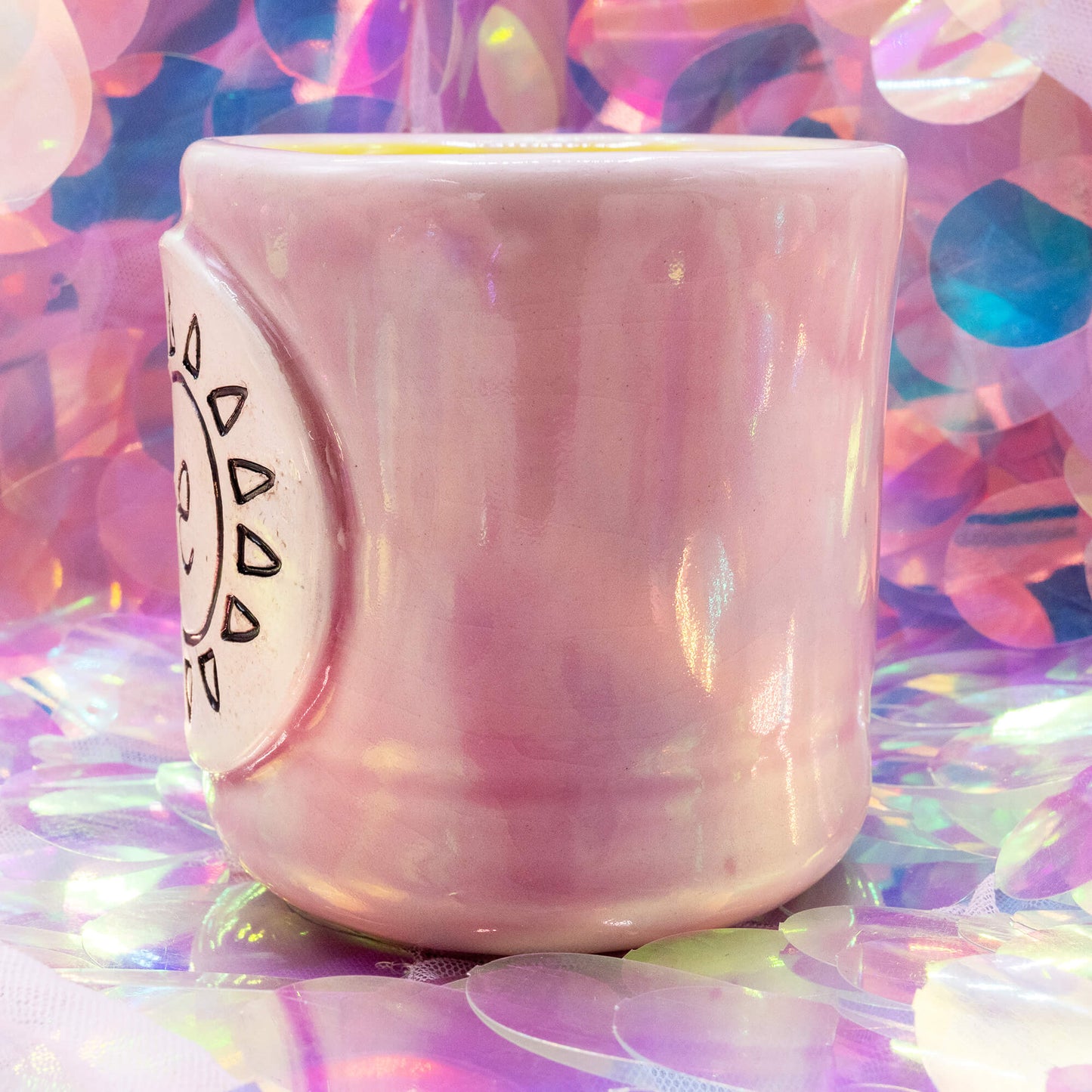 Pale pink handmade ceramic mug with a glossy finish and the Happiness Enchanters sun and symbol plaque, shown on a pastel iridescent background.