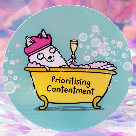A round vinyl sticker by Happiness Enchanters featuring a cute illustrated wolf relaxing in a yellow bubble bath, wearing a pink shower cap and holding a champagne glass. The tub reads “Prioritising Contentment”. The background is soft turquoise with bubbles. Designed by Katie Abey for gentle, magical self care.