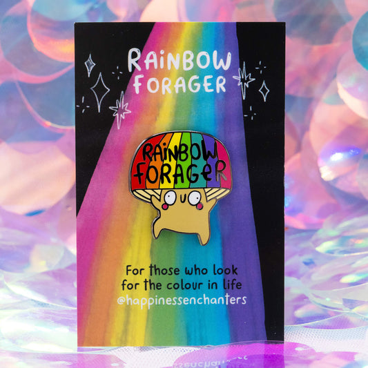 A colourful enamel pin badge shaped like a happy mushroom with a rainbow cap reading “Rainbow Forager,” designed by Katie Abey for Happiness Enchanters. Displayed on a rainbow backing card with the quote “For those who look for the colour in life.”