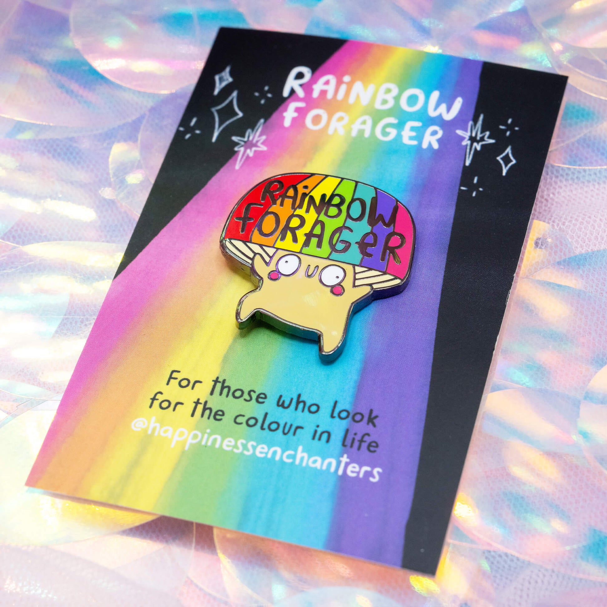 The Rainbow Forager Mushroom Pin Badge by Happiness Enchanters, featuring a cute illustrated mushroom with a rainbow hat and smiling face on a colourful backing card. A joyful accessory for those who love bright, magical art.