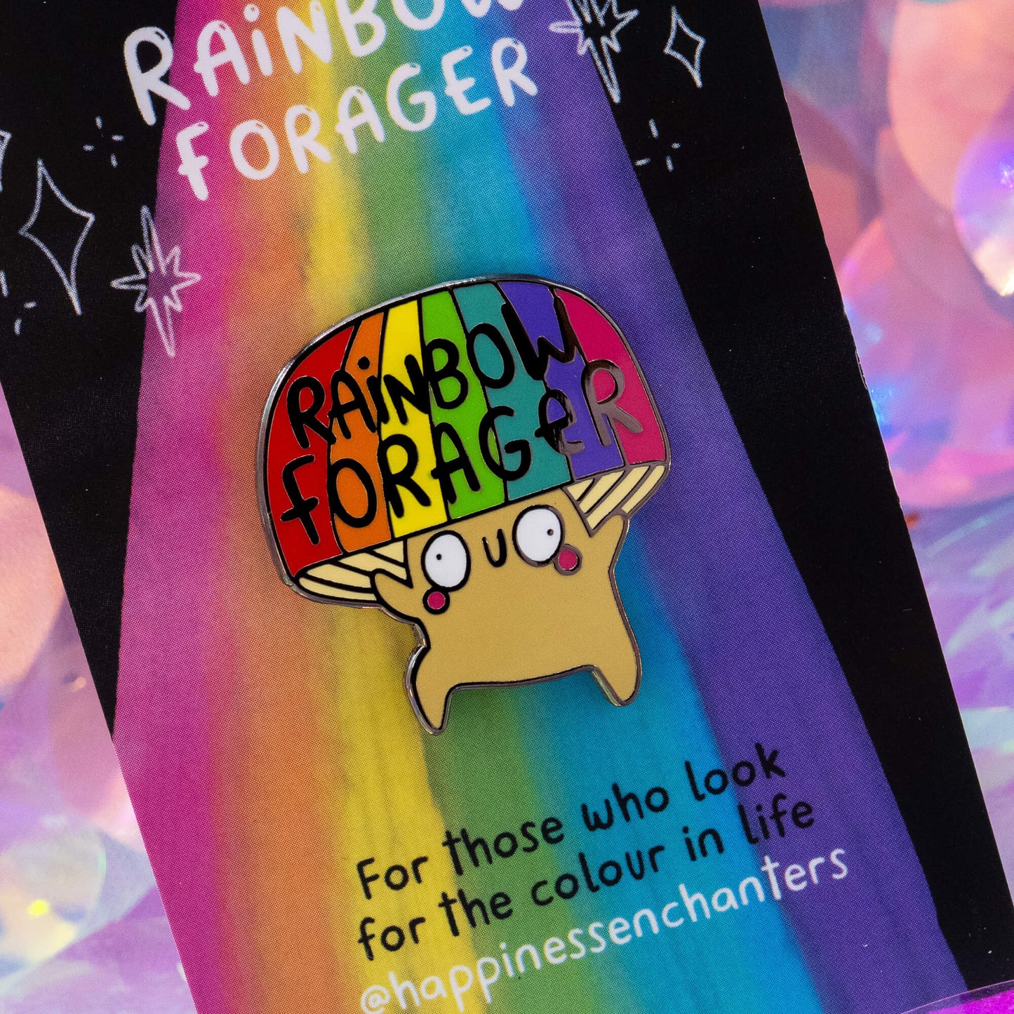 Close-up of the Rainbow Forager Mushroom enamel pin badge by Happiness Enchanters, illustrated by Katie Abey. The cheerful mushroom character has a rainbow cap and a happy expression, symbolising positivity and colour.