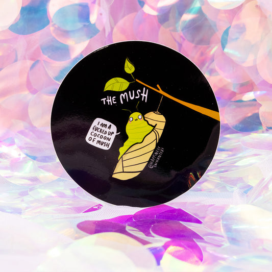 Round black sticker by Happiness Enchanters featuring a bright green caterpillar wrapped in a cocoon, hanging from a branch with leaves. The text reads “The Mush” and the speech bubble says “I am a fucked up cocoon of mush”. Set against a dreamy iridescent pastel background. A humorous mental health themed sticker.