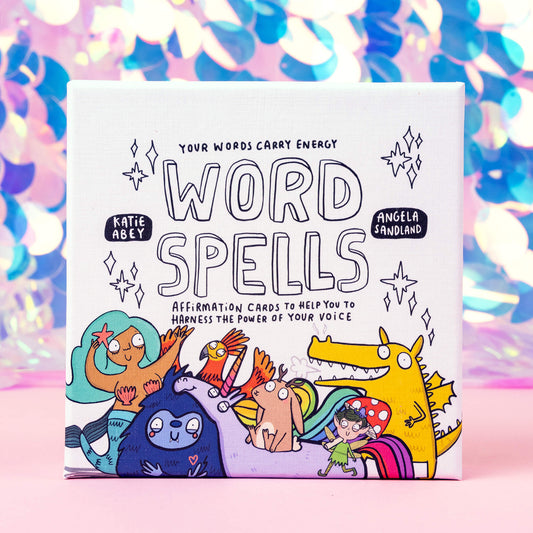 Box of Word Spell Cards on a pink and sparkly background, the box is white with 'your words carry energy' and 'affirmation cards to help you to harness the power of your voice' written on with various illustrations.