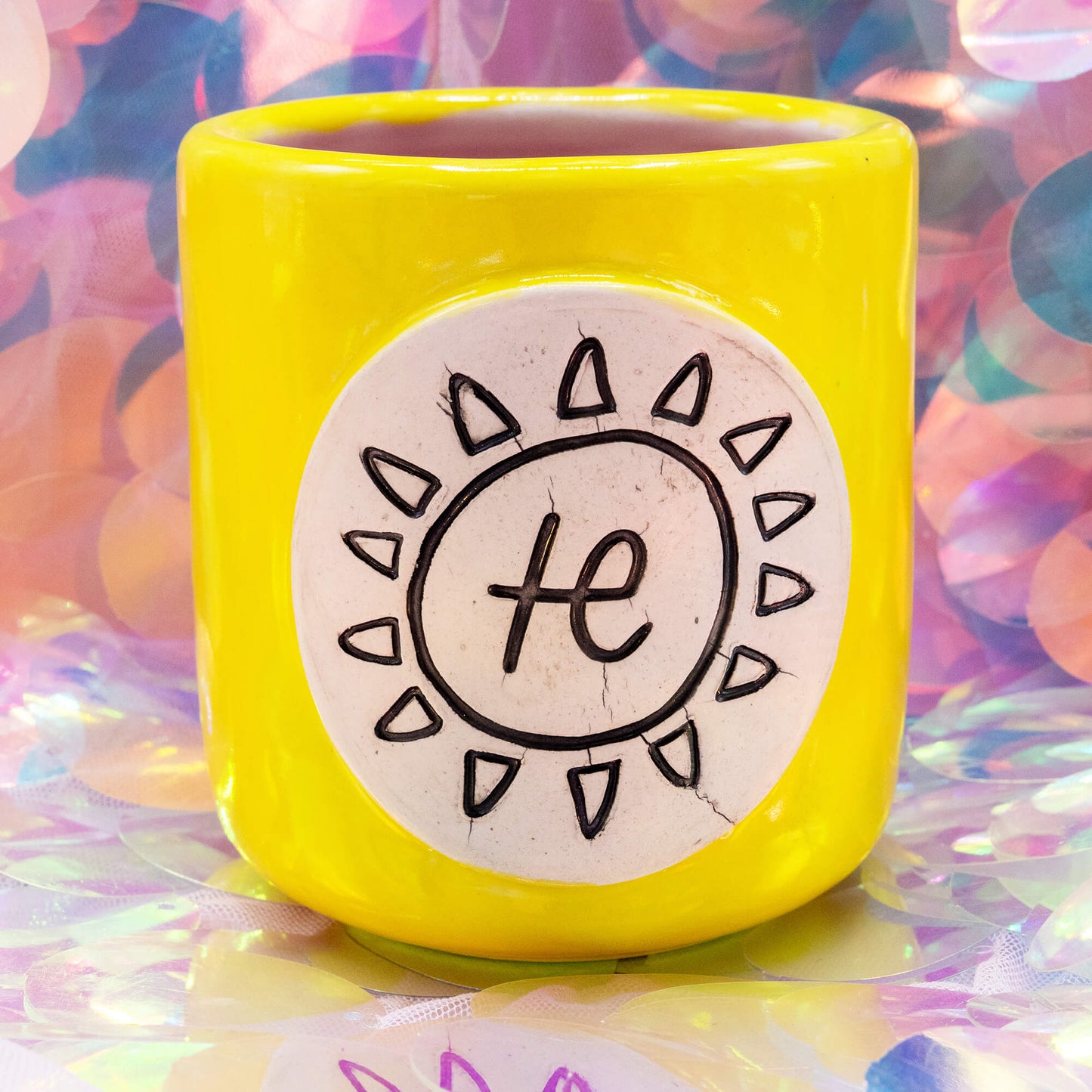 Front view of the yellow Happiness Enchanters ceramic cacao cup with pink interior and sun symbol plaque.