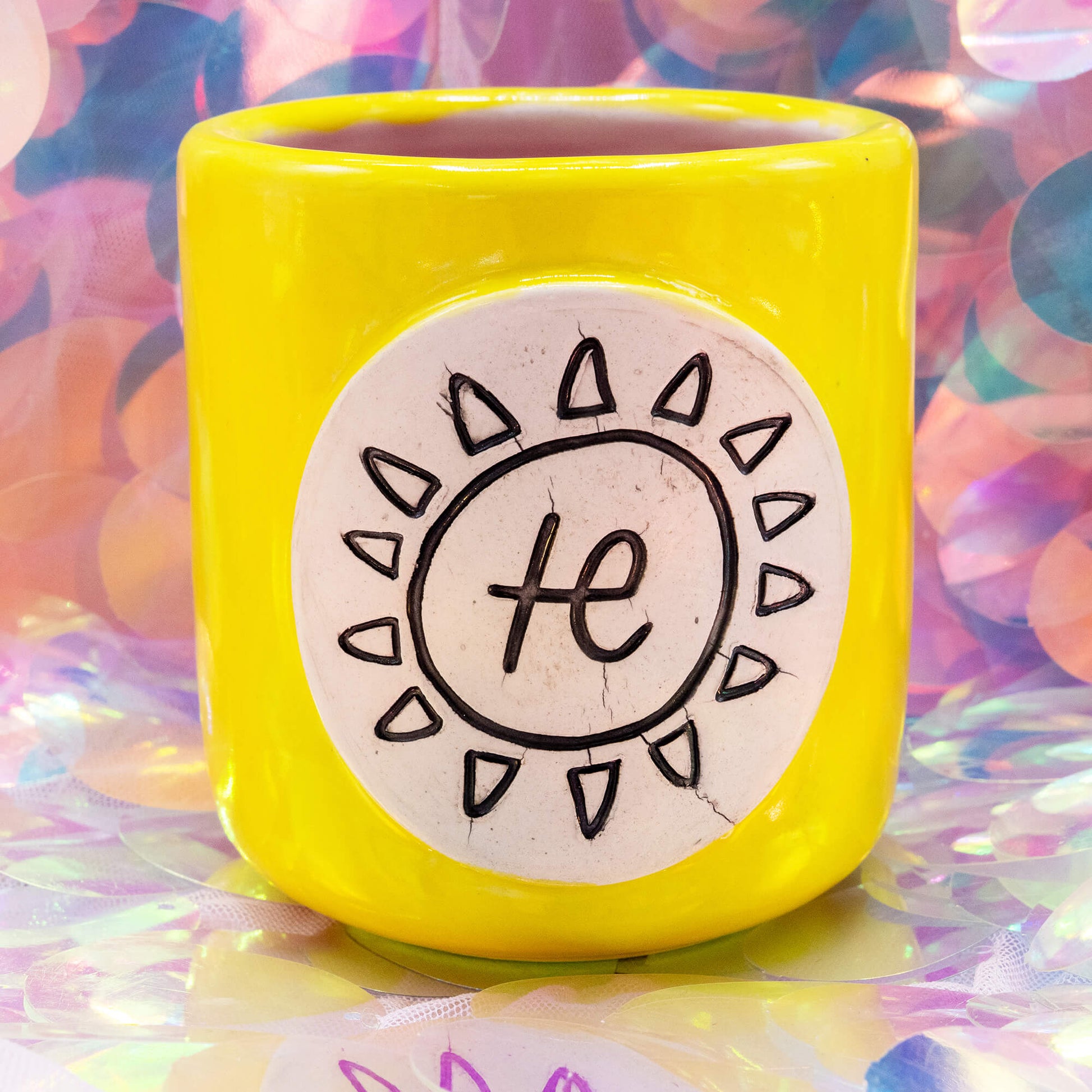 Front view of the yellow Happiness Enchanters ceramic cacao cup with pink interior and sun symbol plaque.