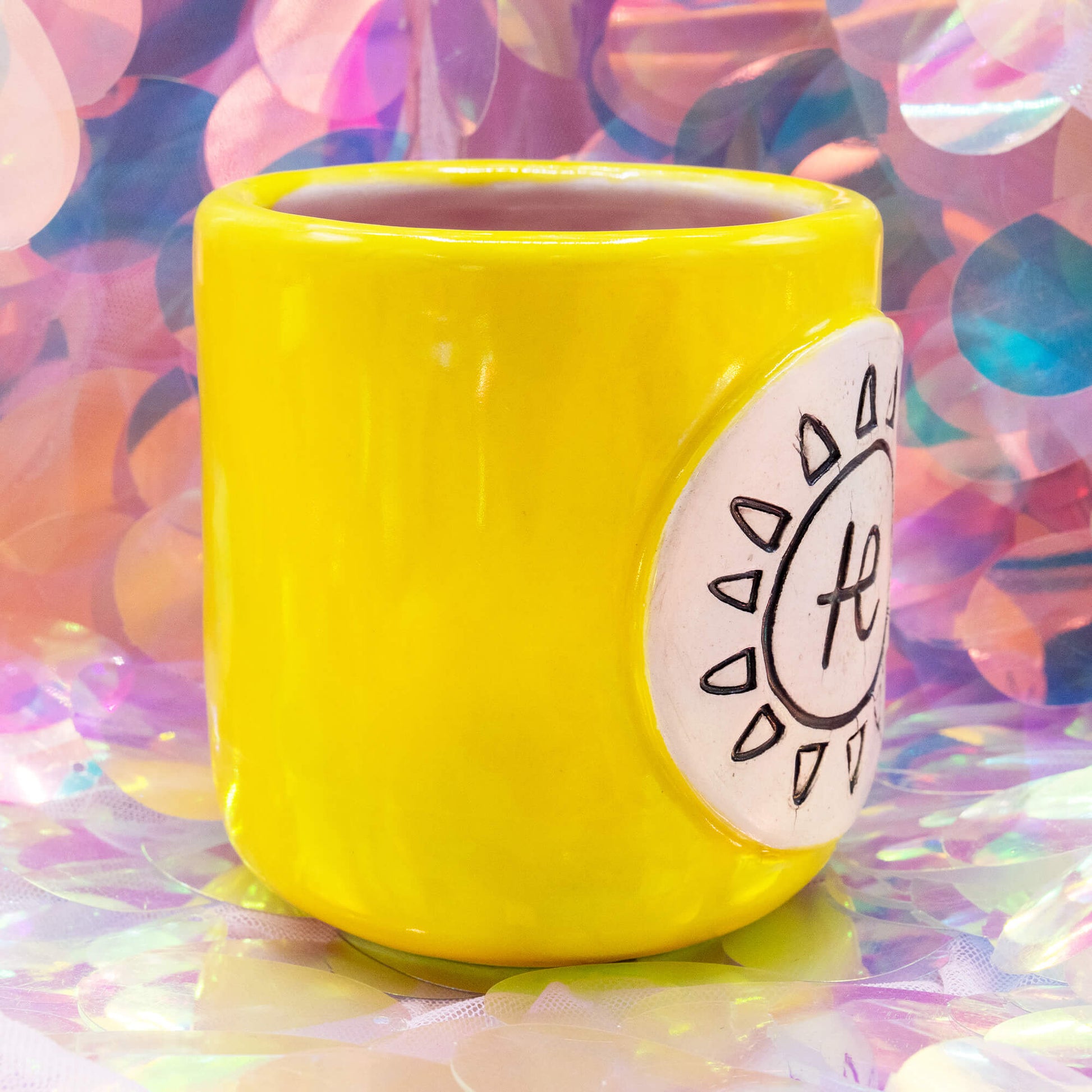 Side angle of the yellow Happiness Enchanters cacao mug with hand-carved sun symbol plaque.